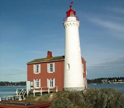 A lighthouse with a white tower and red top, adjacent to a two-story red and white house on a rocky shoreline.