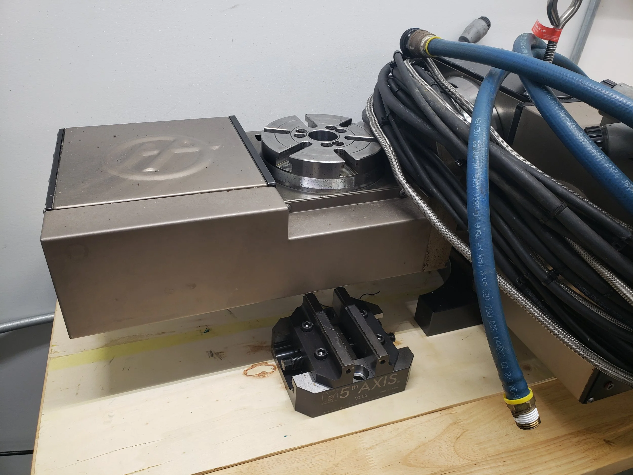 Industrial machinery with several hoses connected to a metal block, mounted on a wooden surface.