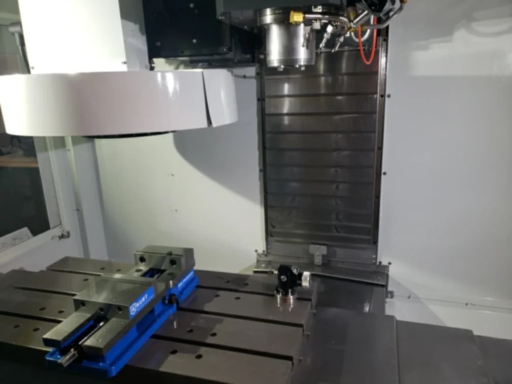 Close-up of a CNC machine worktable with a blue vise, part of an industrial manufacturing setup.