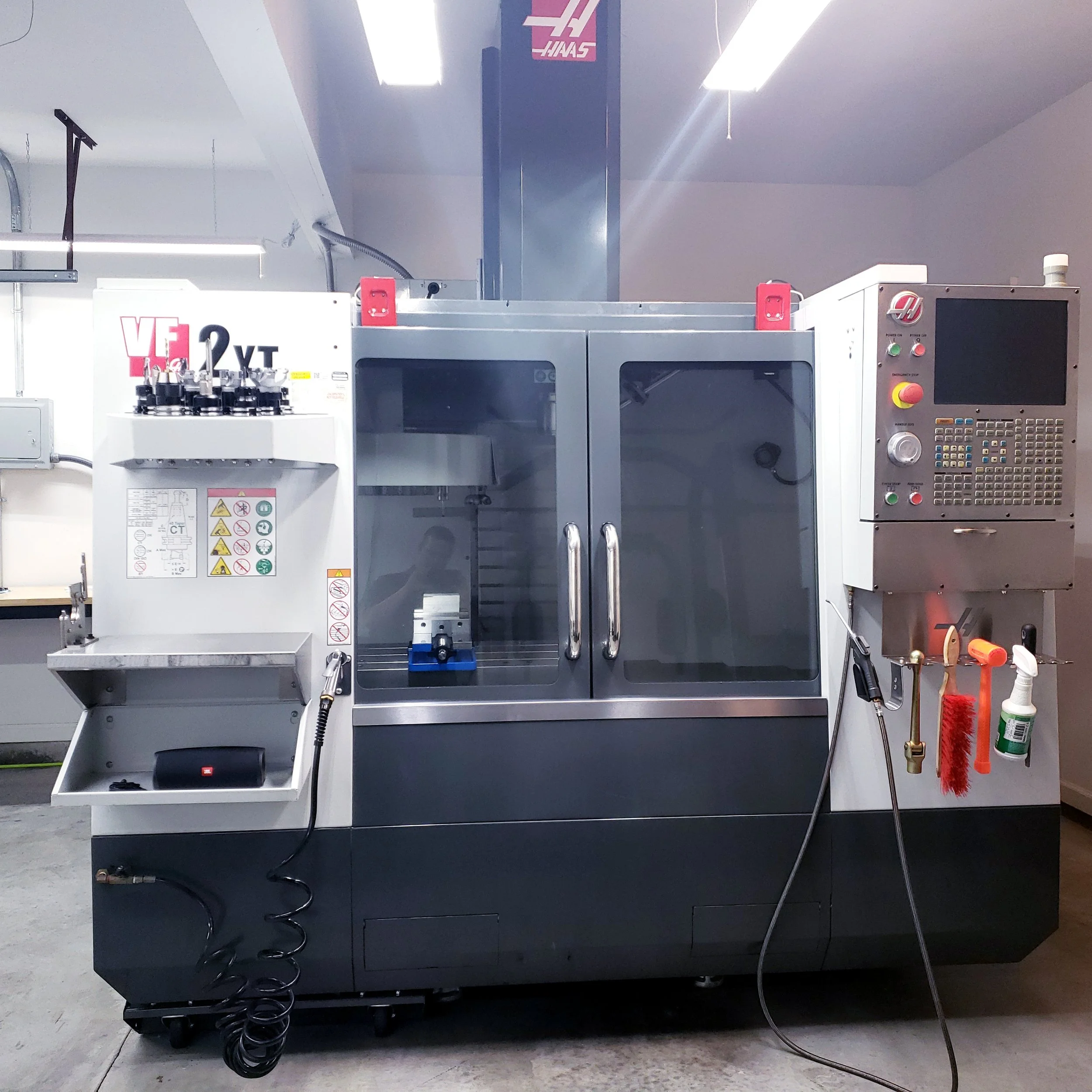 Industrial CNC machine with control panel and safety tools attached, located in a manufacturing setting.