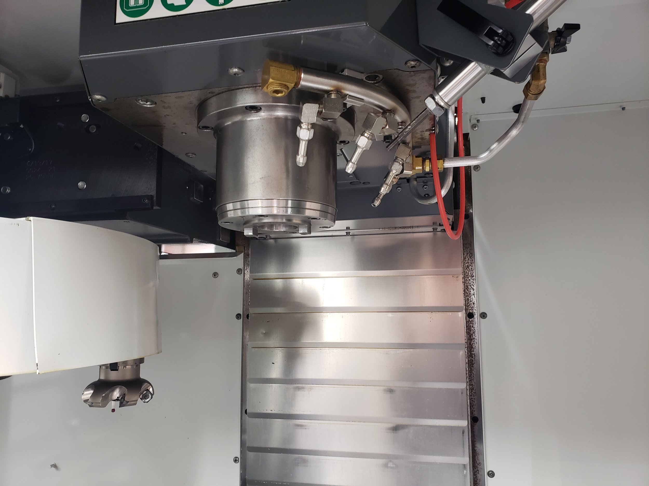 Close-up view of a CNC machine spindle and tool holder with attached hydraulic and air hoses.