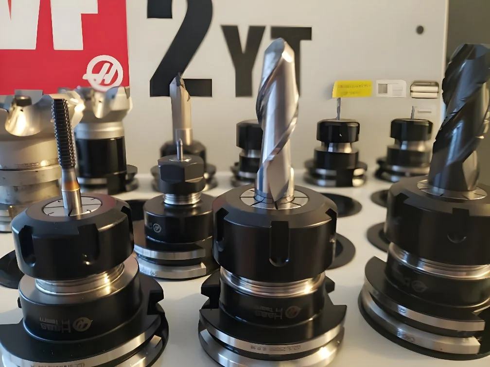 A display of various CNC end mills and drill bits attached to tool holders, arranged on a white surface with labels and signs in the background.