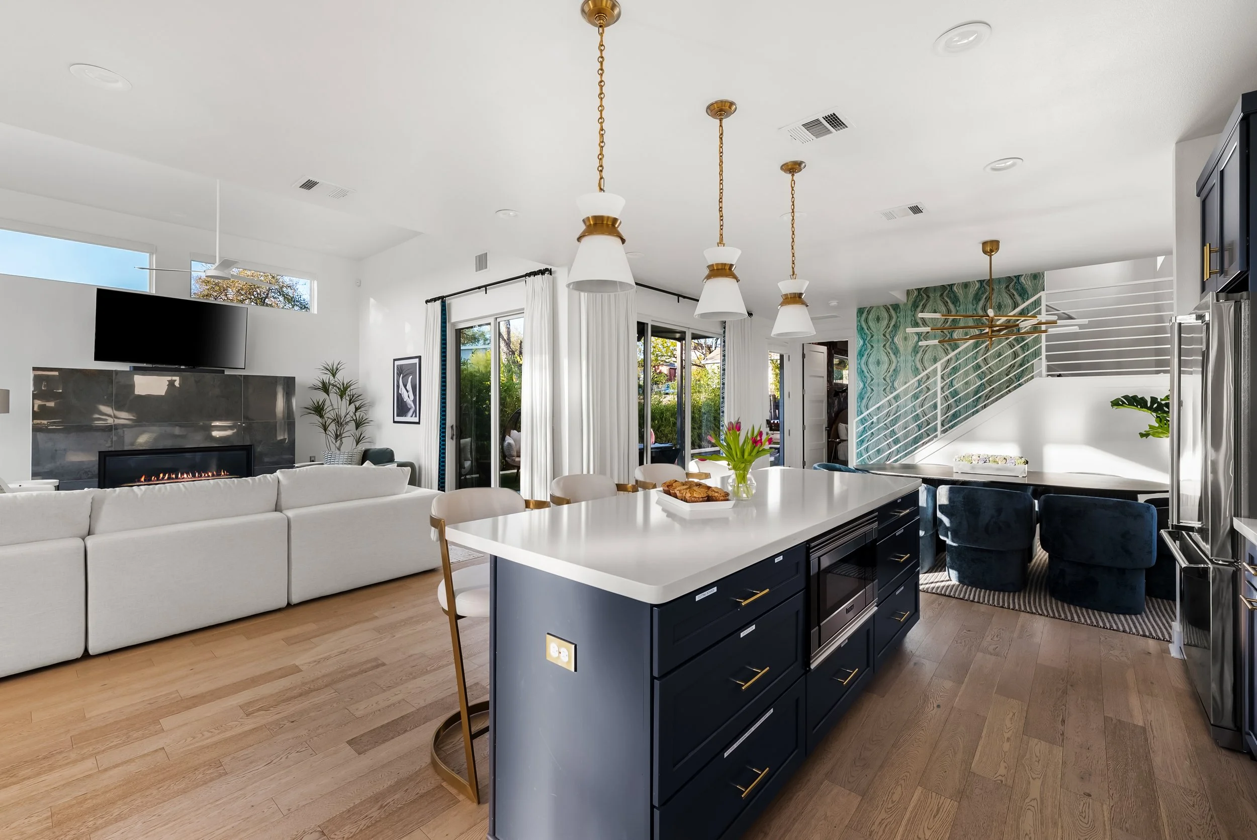 Open-concept living room and kitchen with white walls, dark blue kitchen island, white countertops, pendant lights, sliding glass doors, and a fireplace