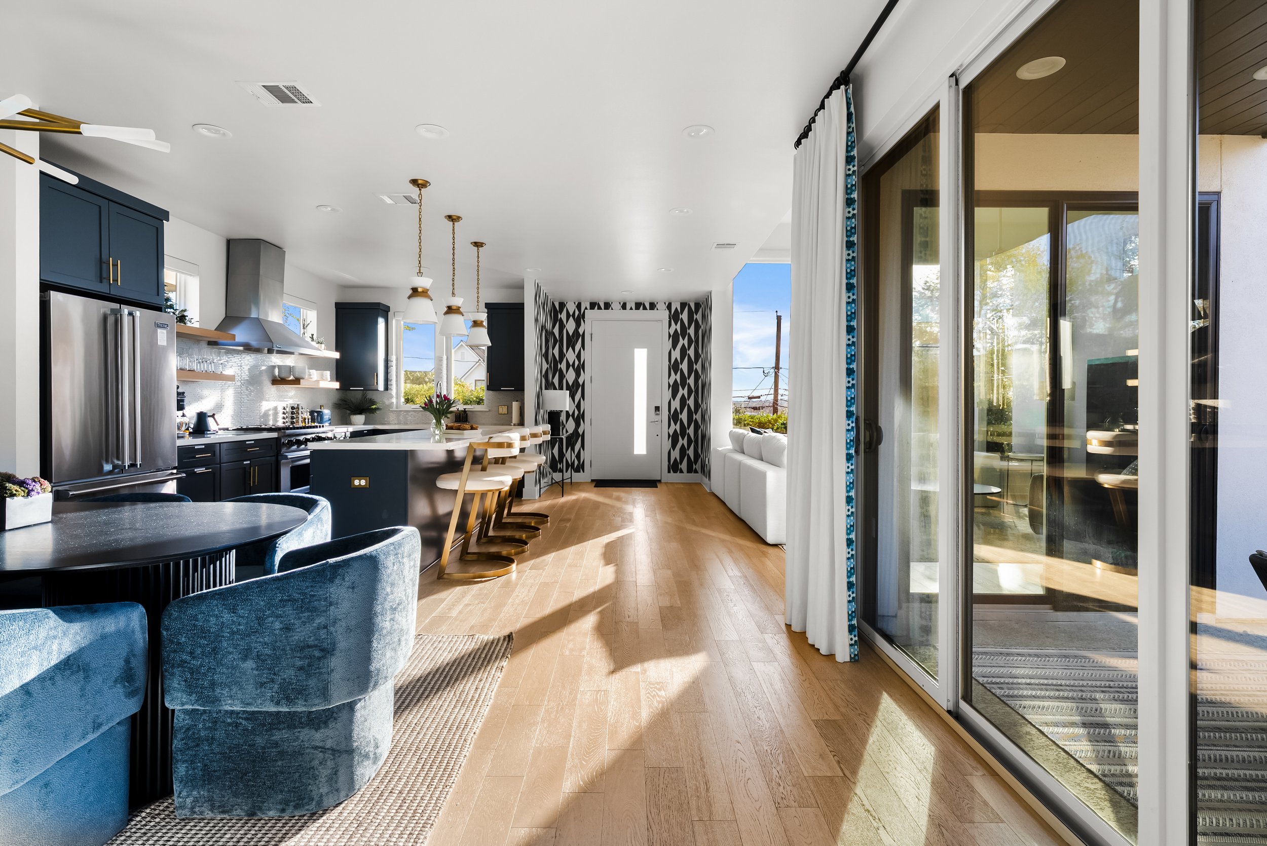 Open-concept kitchen and living area with blue cabinets, stainless steel appliances, island with bar stools, and sliding glass doors.