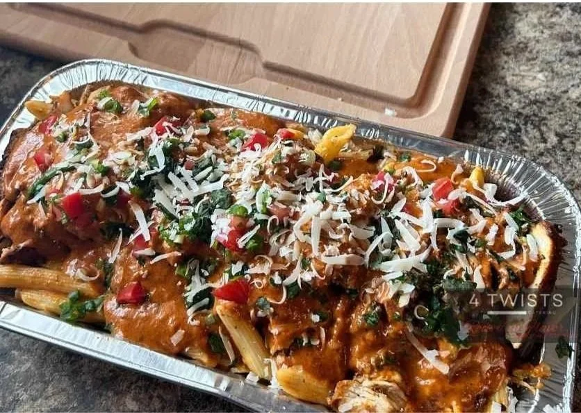 Tray of baked pasta topped with tomato sauce, shredded cheese, chopped herbs, and diced tomatoes.