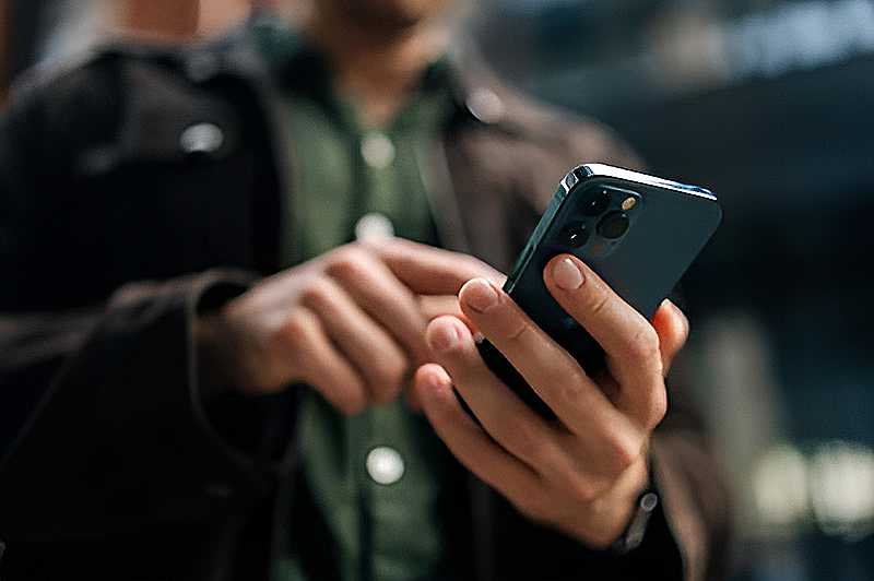 Person holding a smartphone with a dark green case, wearing a brown jacket and green shirt.
