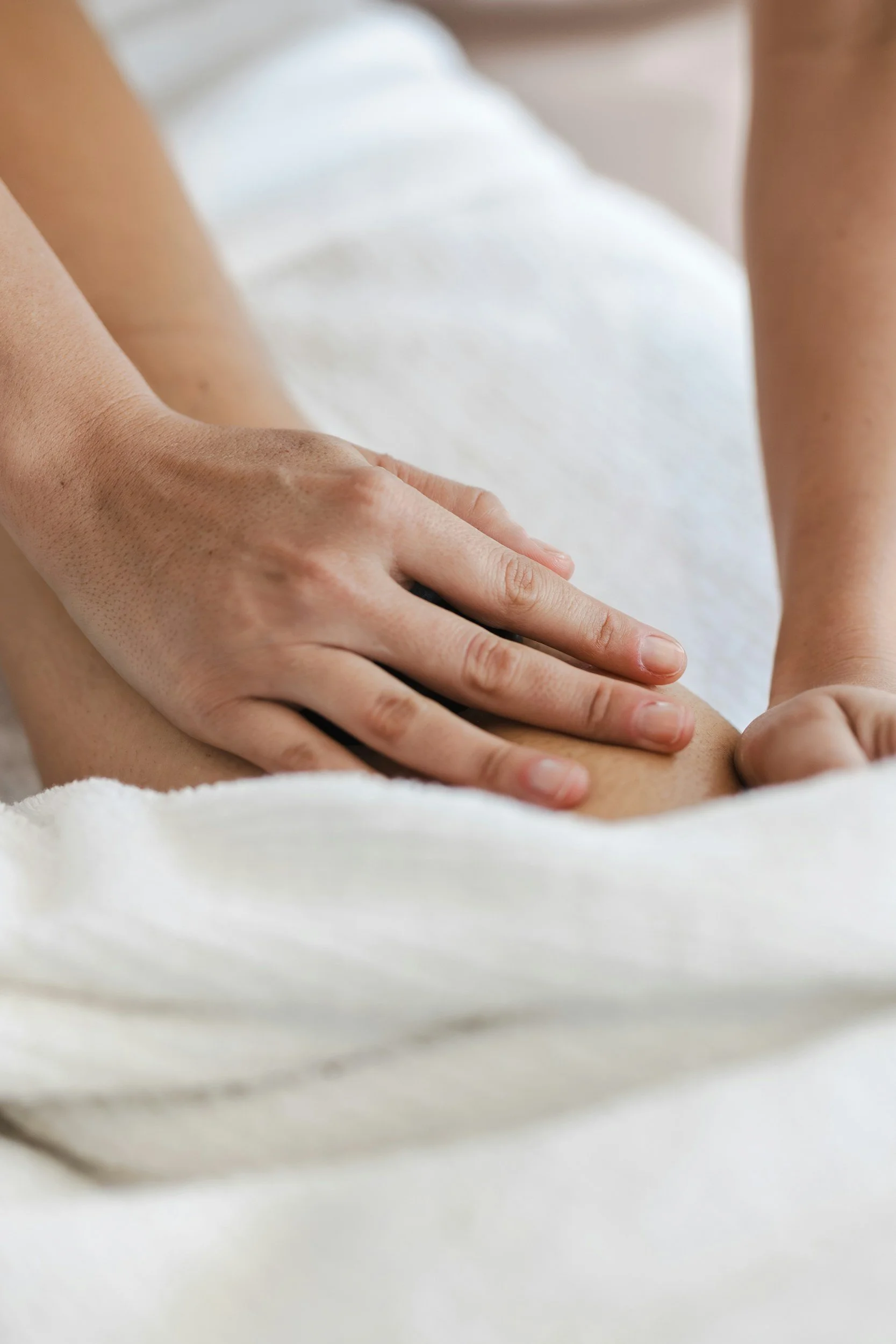 Close-up of a person's hand gently touching a patient's leg during a massage or physical therapy session, both lying on a white towel.