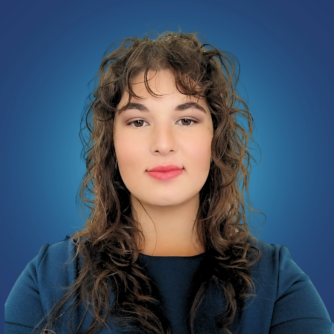 A woman with curly brown hair and light makeup, wearing a dark top, poses against a blue gradient background.