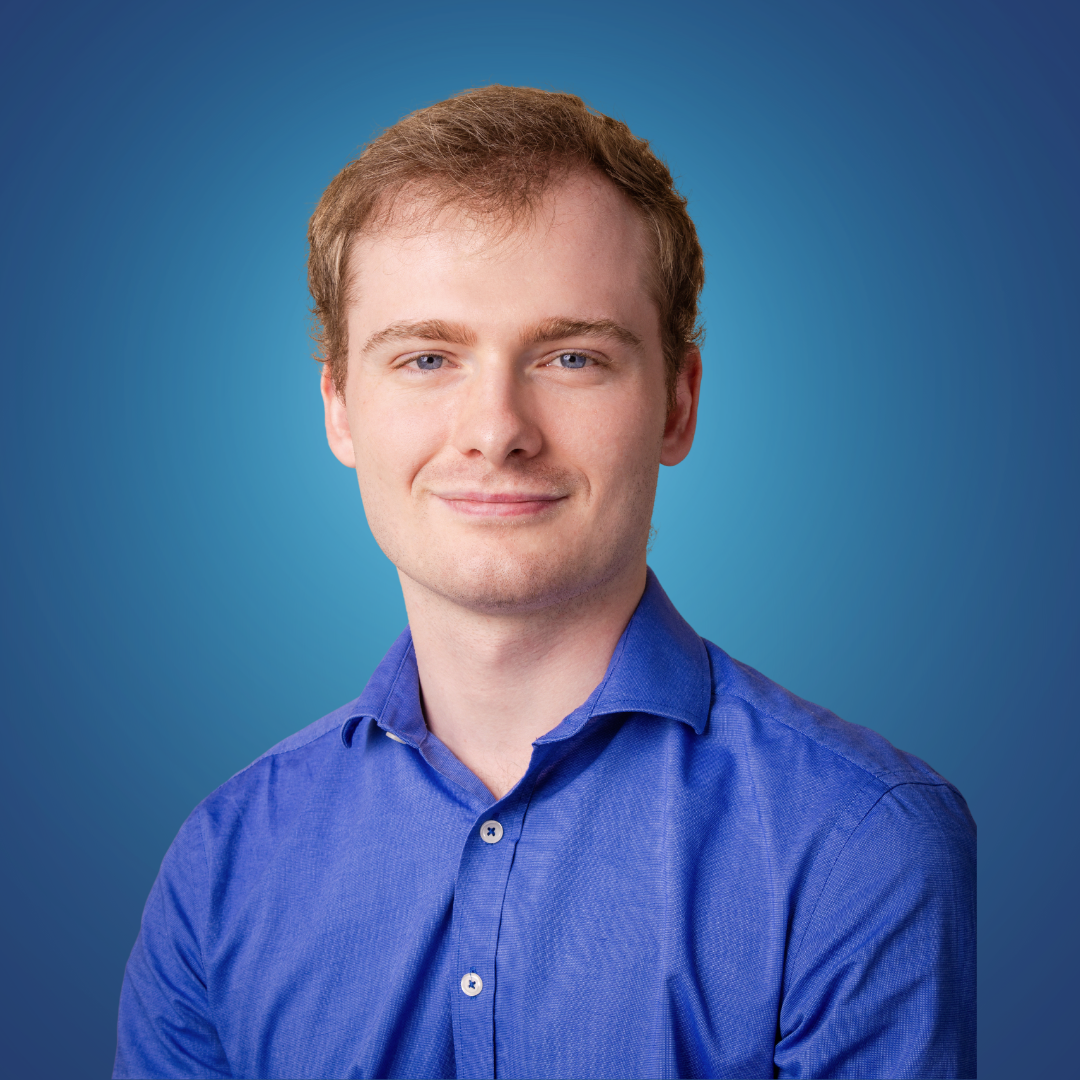 Portrait of a young man with short light brown hair, blue eyes, wearing a blue dress shirt, against a blue gradient background.