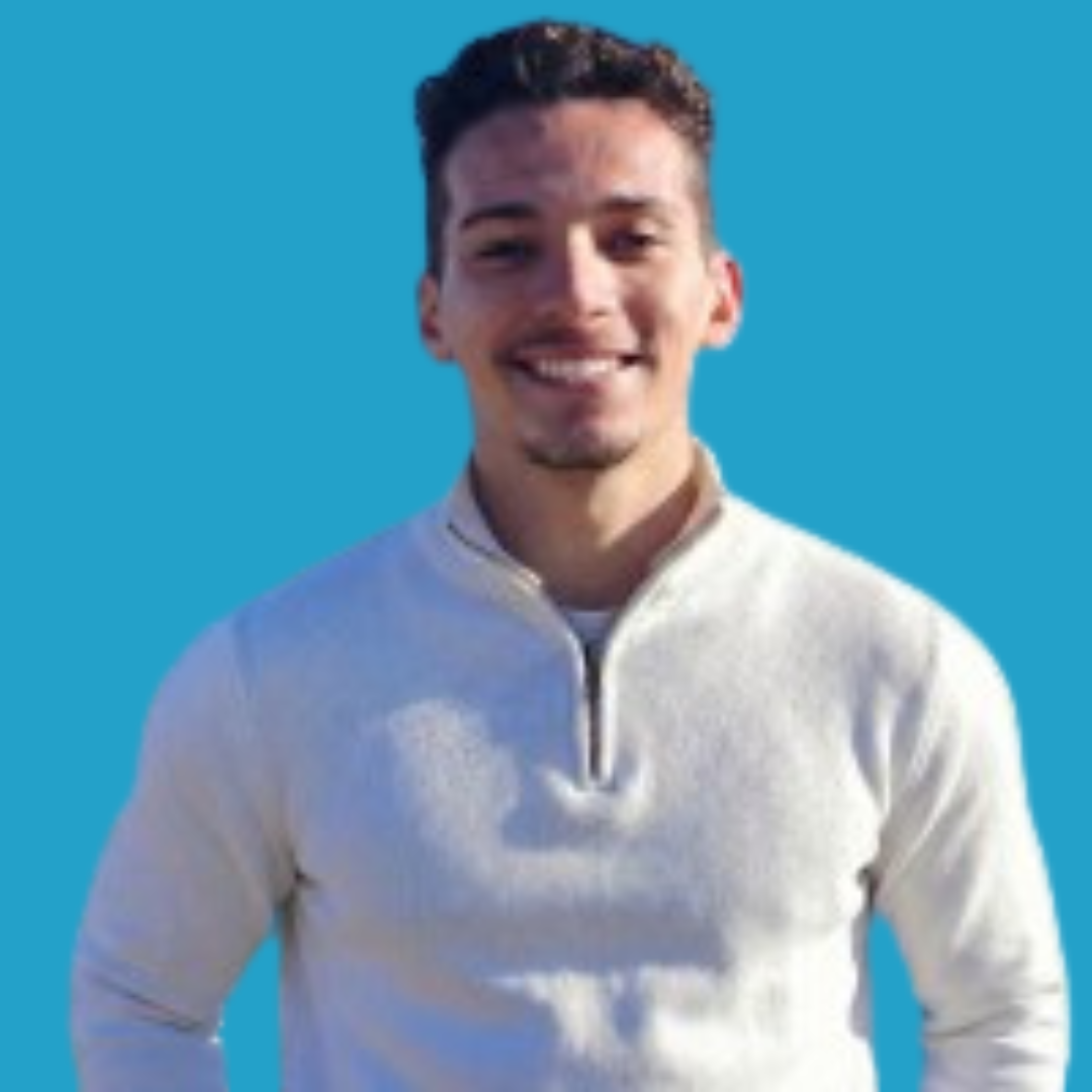 A young man smiling against a bright blue background, wearing a light-colored zip-up sweater.