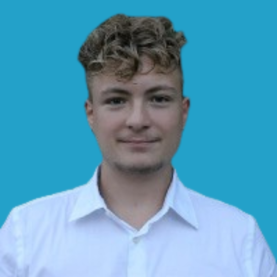 A young man with light skin, short curly brown hair, wearing a white collared shirt, standing against a blue background.
