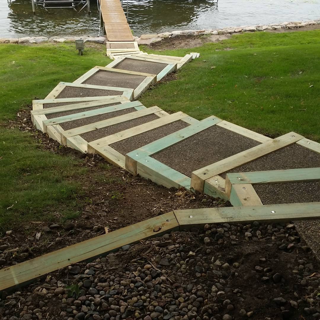 A zigzagging wooden walkway built alongside a grassy area near a body of water, leading to a dock with a ramp.