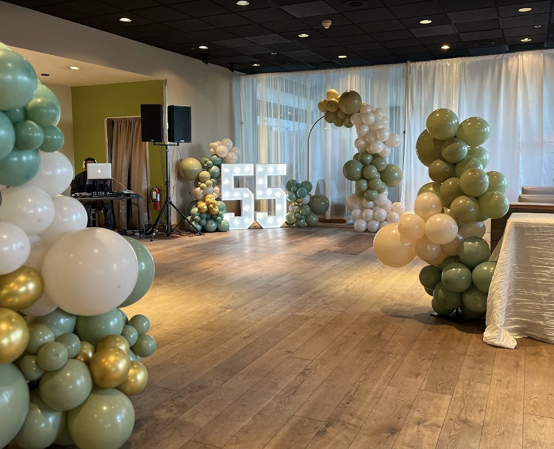 Event space decorated with pastel-colored balloon arrangements, large illuminated number 55, and a DJ station in the corner.