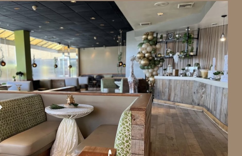 Interior of a restaurant decorated for a celebration with a balloon arrangement and holiday decor, featuring booths, a bar area, and large windows.