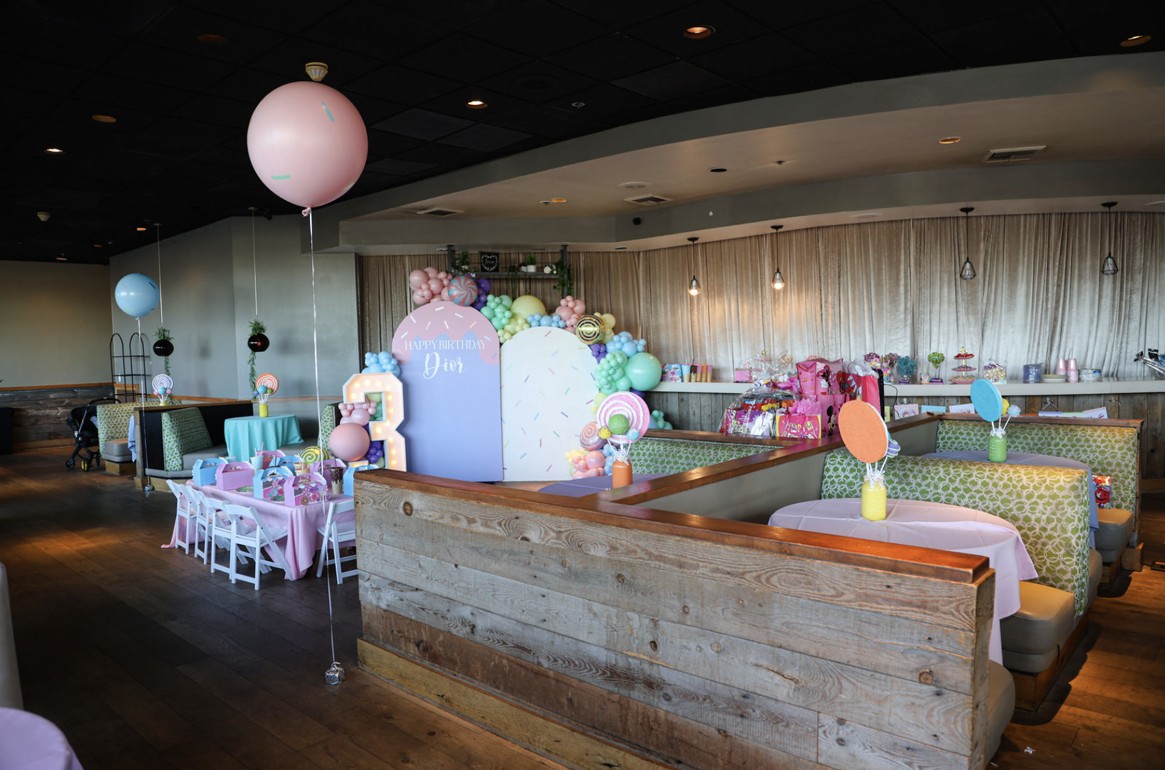 Colorful birthday party setup with balloons, decorated tables, and gift boxes in a restaurant or event space.