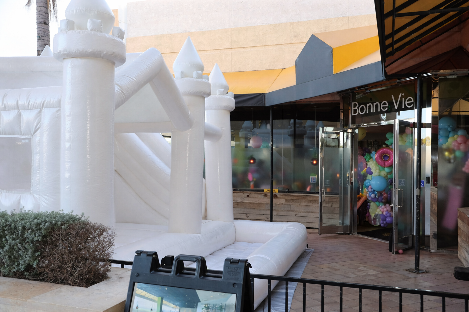 Inflatable castle outside a building with glass doors, balloons inside, and a sign that reads "Bonne Vie."