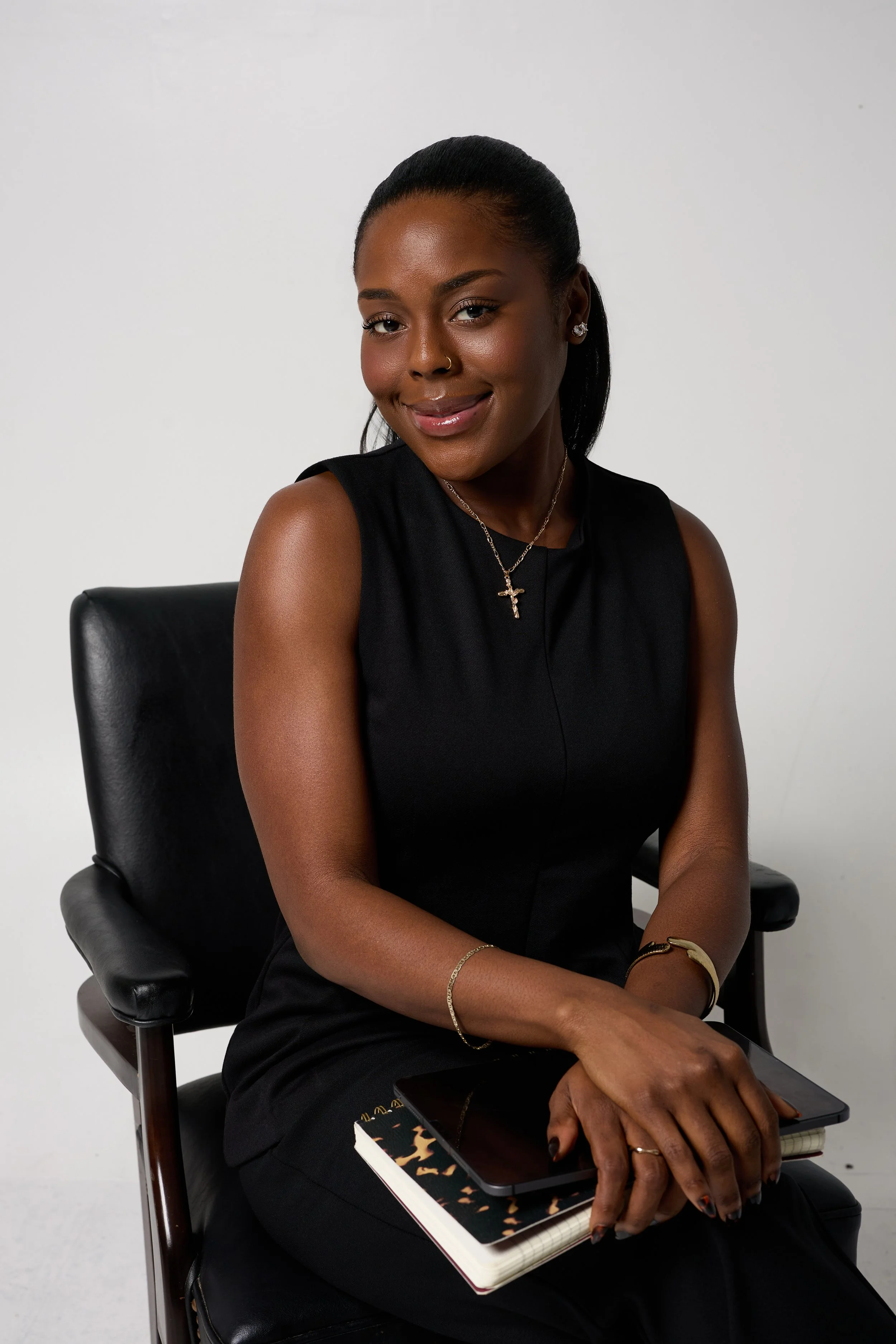 Photo of a woman in a chair smiling with all black on holding a notebook and iPad.