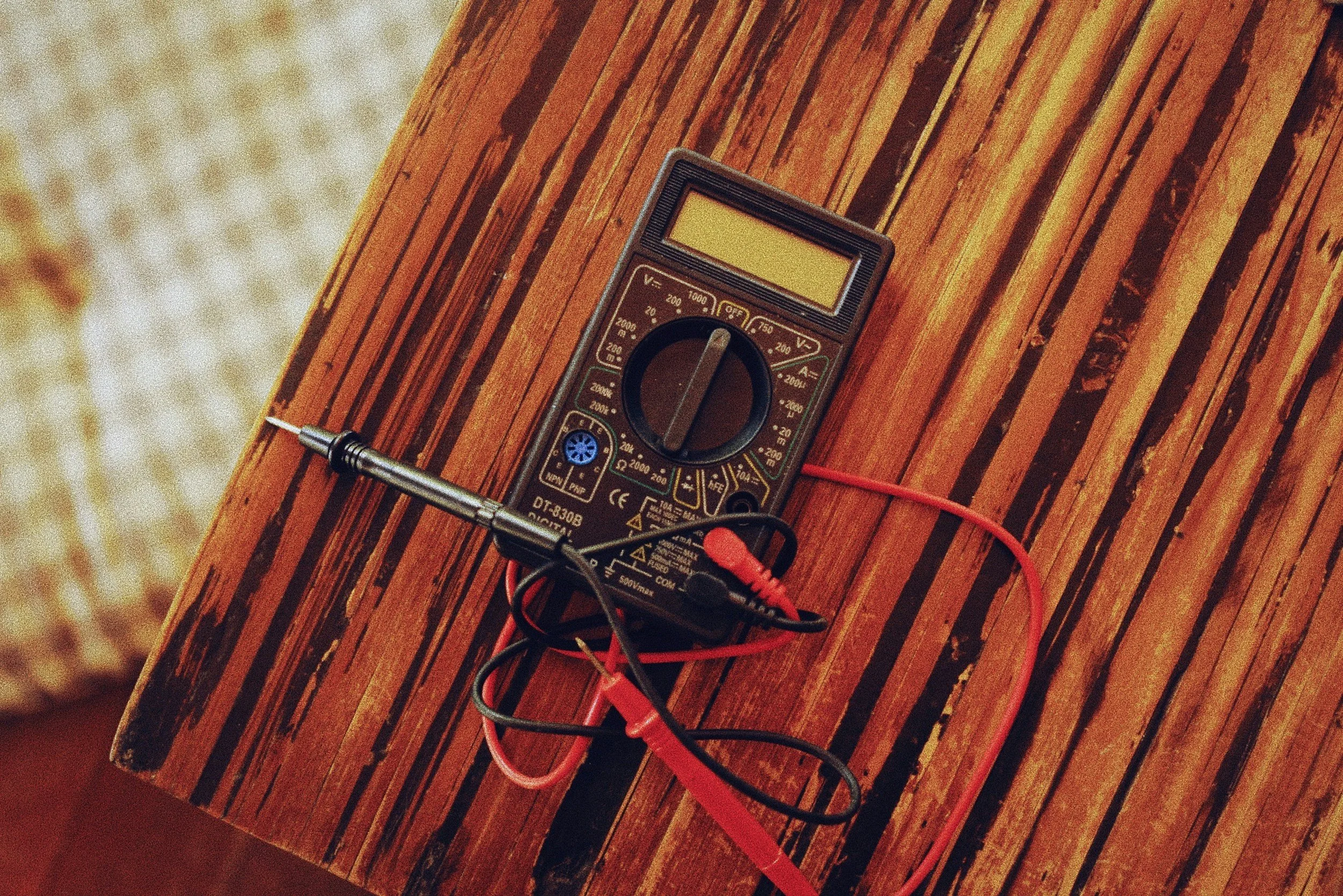 A digital multimeter placed on a wooden surface with red and black probes connected.