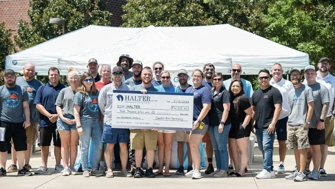 Group of people standing in front of a white tent, holding a large check for $4,000, outdoors on a sunny day.