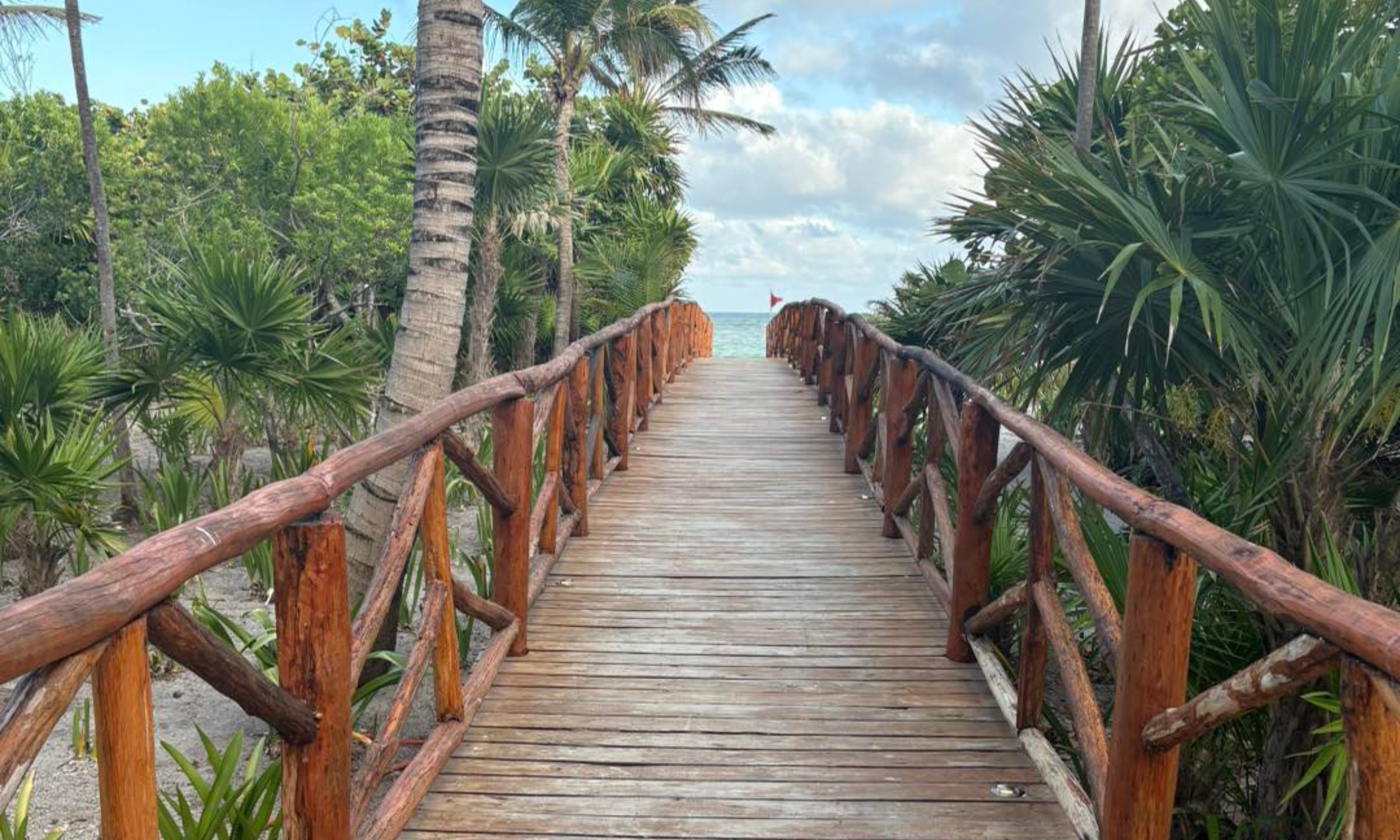 Wooden beach walkway leading to ocean, symbolizing bucket list travel planned by a Northwest Indiana travel agent.