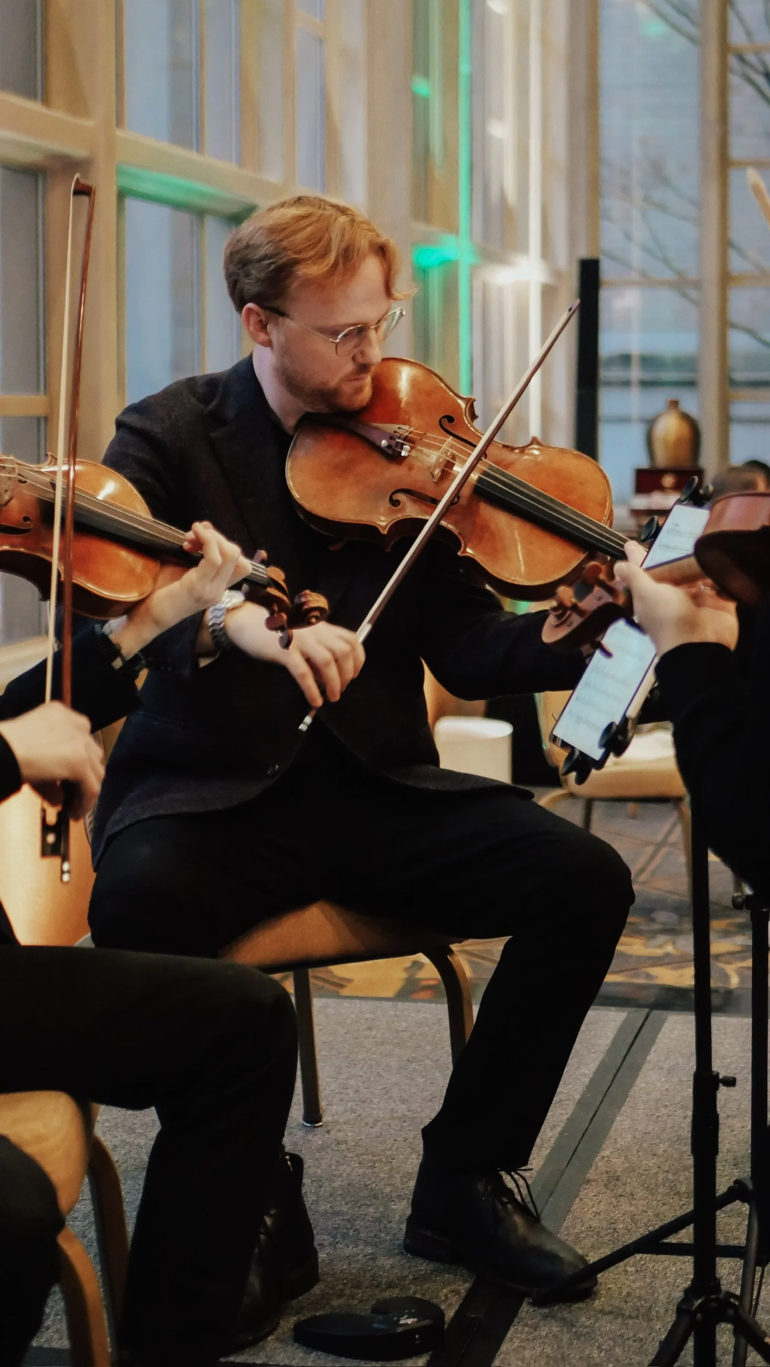 A man with glasses and reddish hair playing a violin during a musical performance indoors.