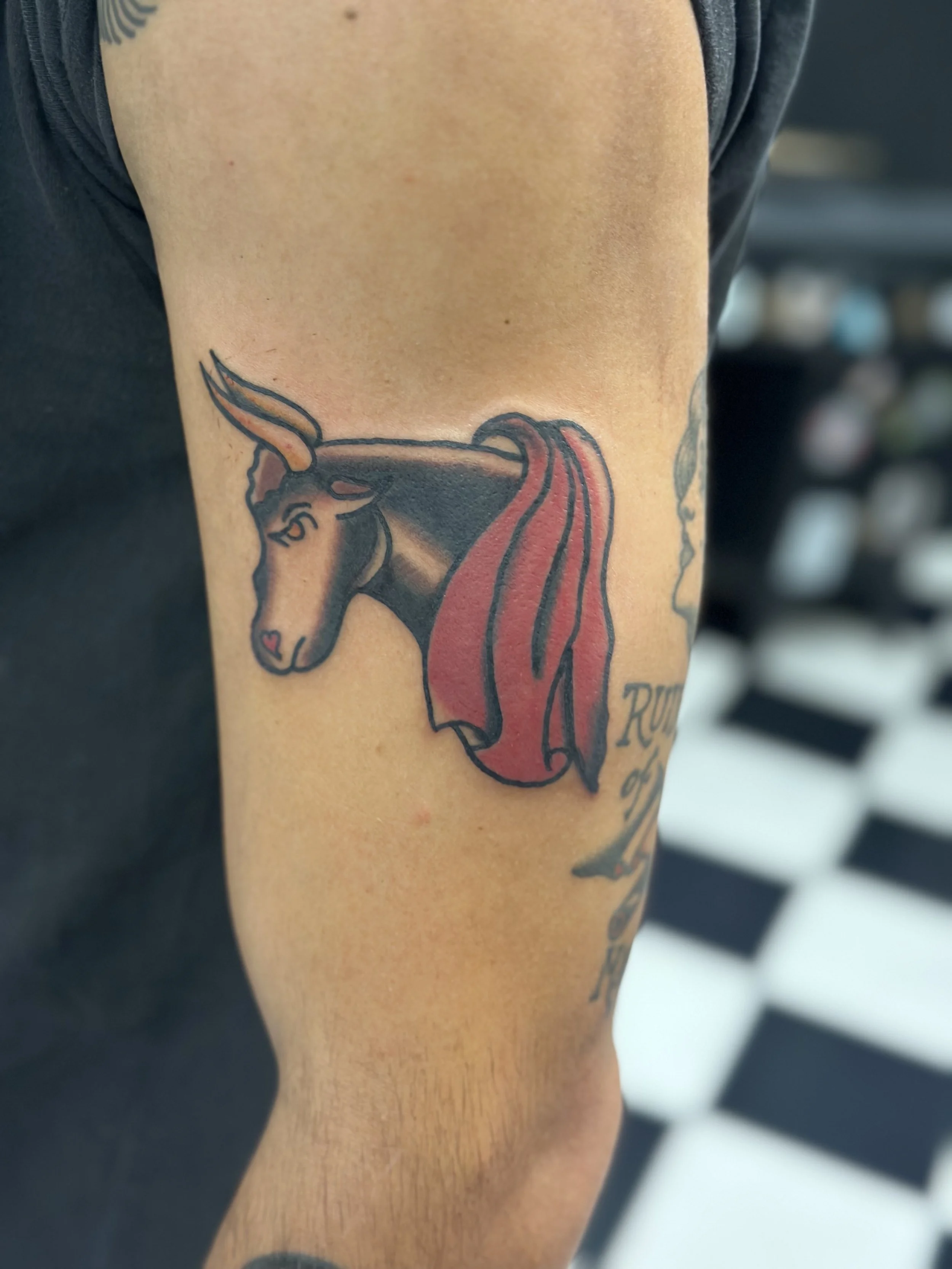 Traditional American color upper arm tattoo featuring a bold black bull head with golden horns and a flowing red mane, custom tattoo by Dan at Big Kahuna Tattoo in Boca Raton, FL.