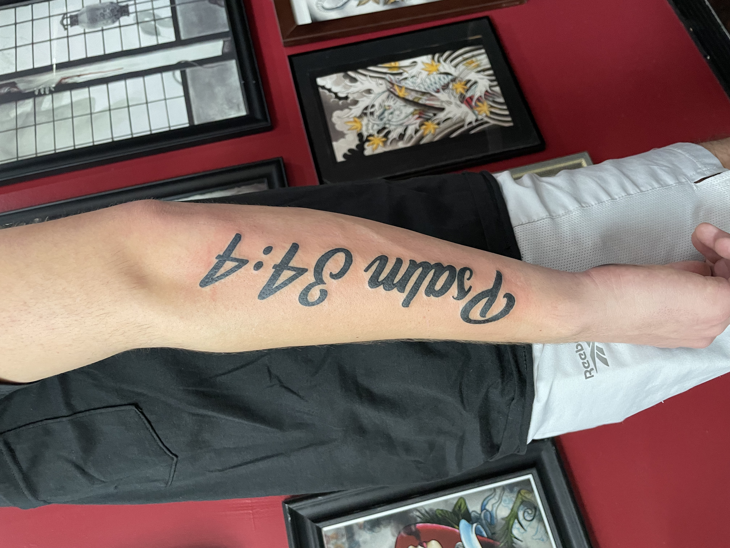 Bold black script forearm tattoo reading "Psalm 34:4" in large flowing cursive lettering running vertically along the arm, custom religious tattoo by Nick at Big Kahuna Tattoo in Boca Raton, FL.