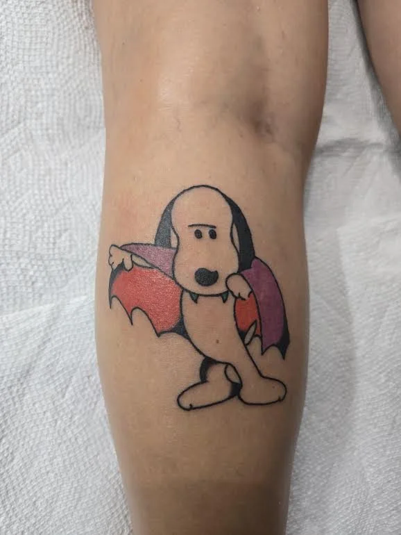 Color traditional leg tattoo featuring Snoopy dressed as a vampire with red and purple bat wings, fun pop culture custom tattoo by Brandon Perez at Big Kahuna Tattoo in Boca Raton, FL