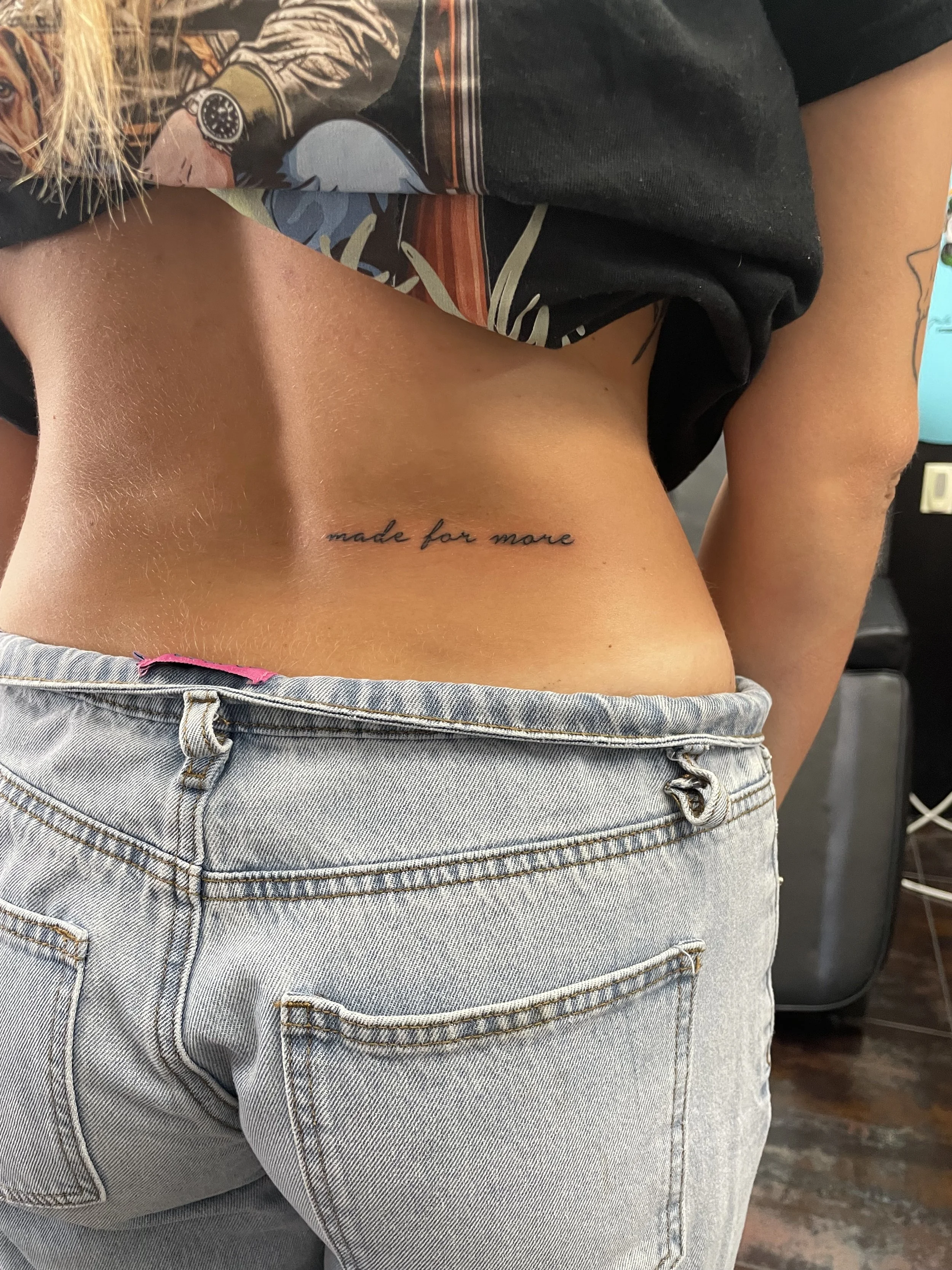 Fine line lower back tattoo featuring the phrase "made for more" in delicate cursive lettering centered along the lower spine, custom tattoo by Nick at Big Kahuna Tattoo in Boca Raton, FL.