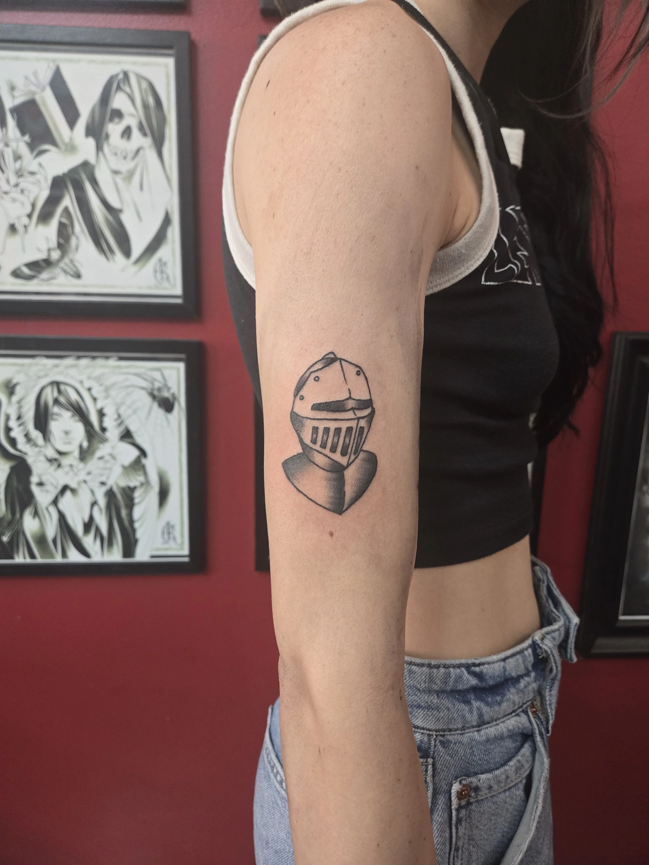 Black and grey traditional upper arm tattoo featuring a bold medieval knight helmet with visor and shoulder plate, custom tattoo by Brandon Perez at Big Kahuna Tattoo in Boca Raton, FL