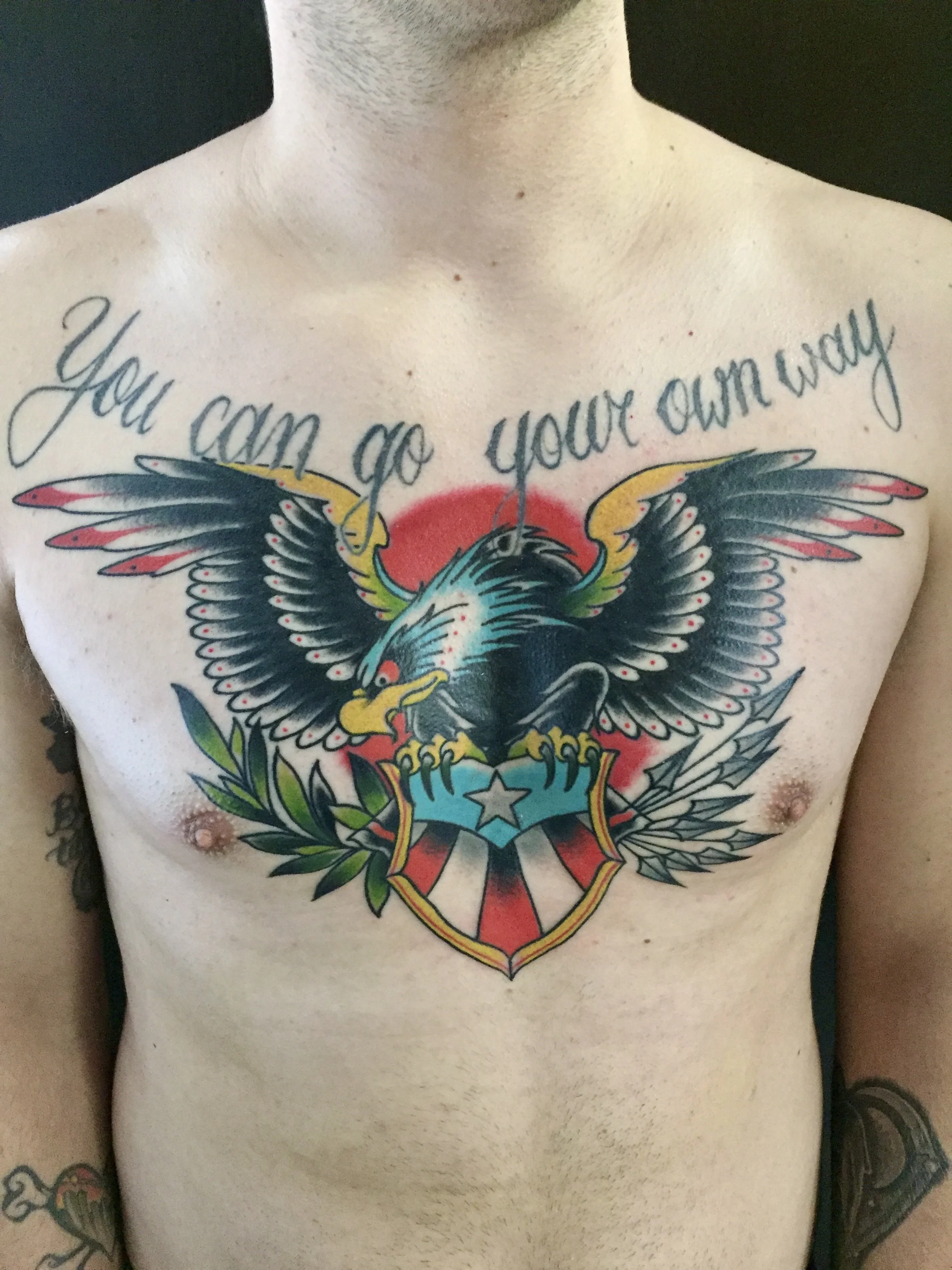 Traditional American color chest piece featuring a bold bald eagle with spread wings clutching a patriotic shield with a star, olive branch, and arrows, custom tattoo by Nick at Big Kahuna Tattoo in Boca Raton, FL.