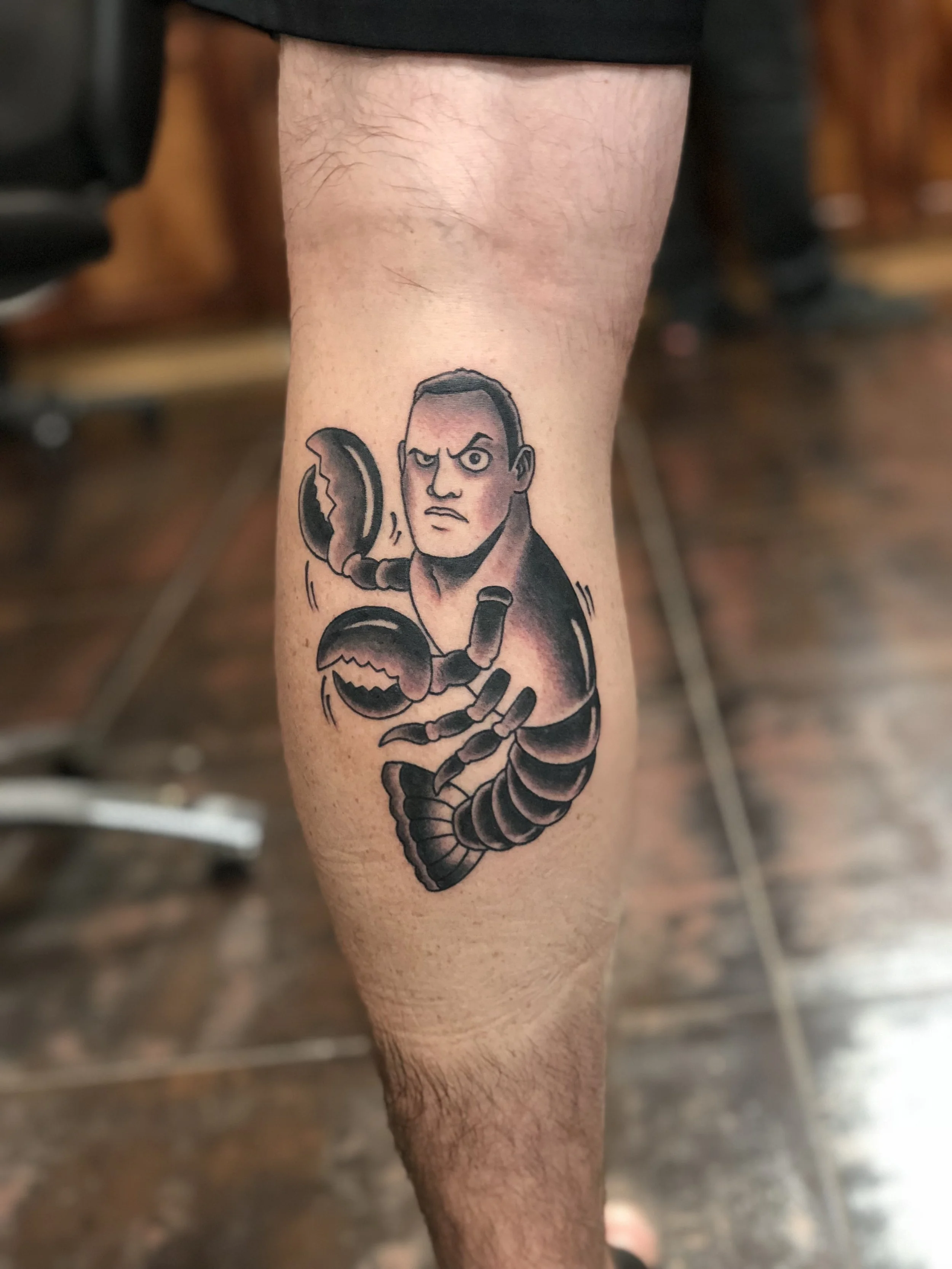Traditional American black and grey leg tattoo featuring a humorous caricature of a Dwayne "the Rock" Johnson's face on a lobster's body. Comedically referencing the song by the B-52's "Rock Lobster" custom tattoo by Nick at Big Kahuna Tattoo in Boca