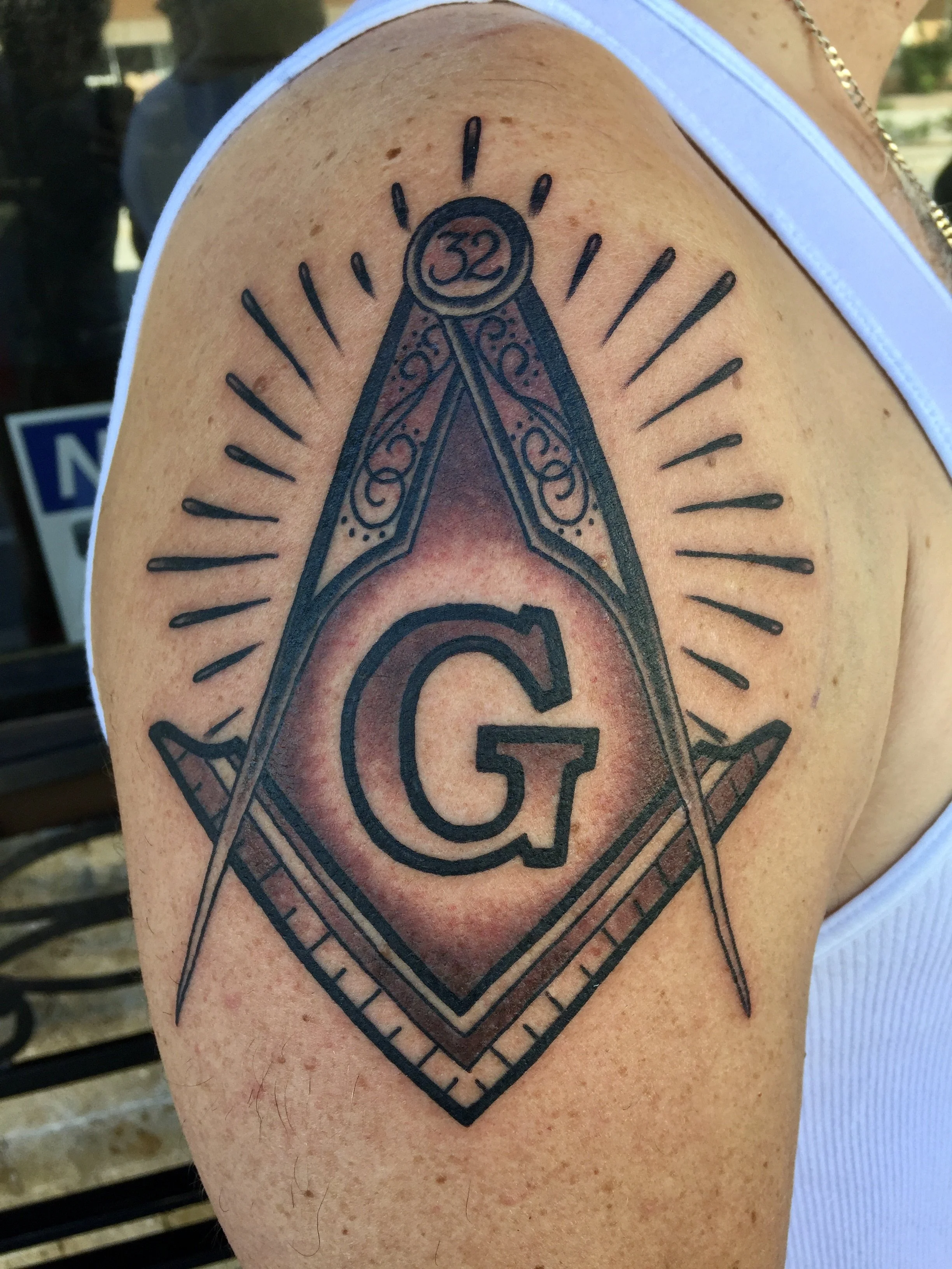 Traditional American black and grey shoulder tattoo featuring the Freemason square and compass symbol with the letter G and the number 32, denoting the 32nd degree of Scottish Rite Freemasonry, custom tattoo by Nick at Big Kahuna Tattoo in Boca Raton