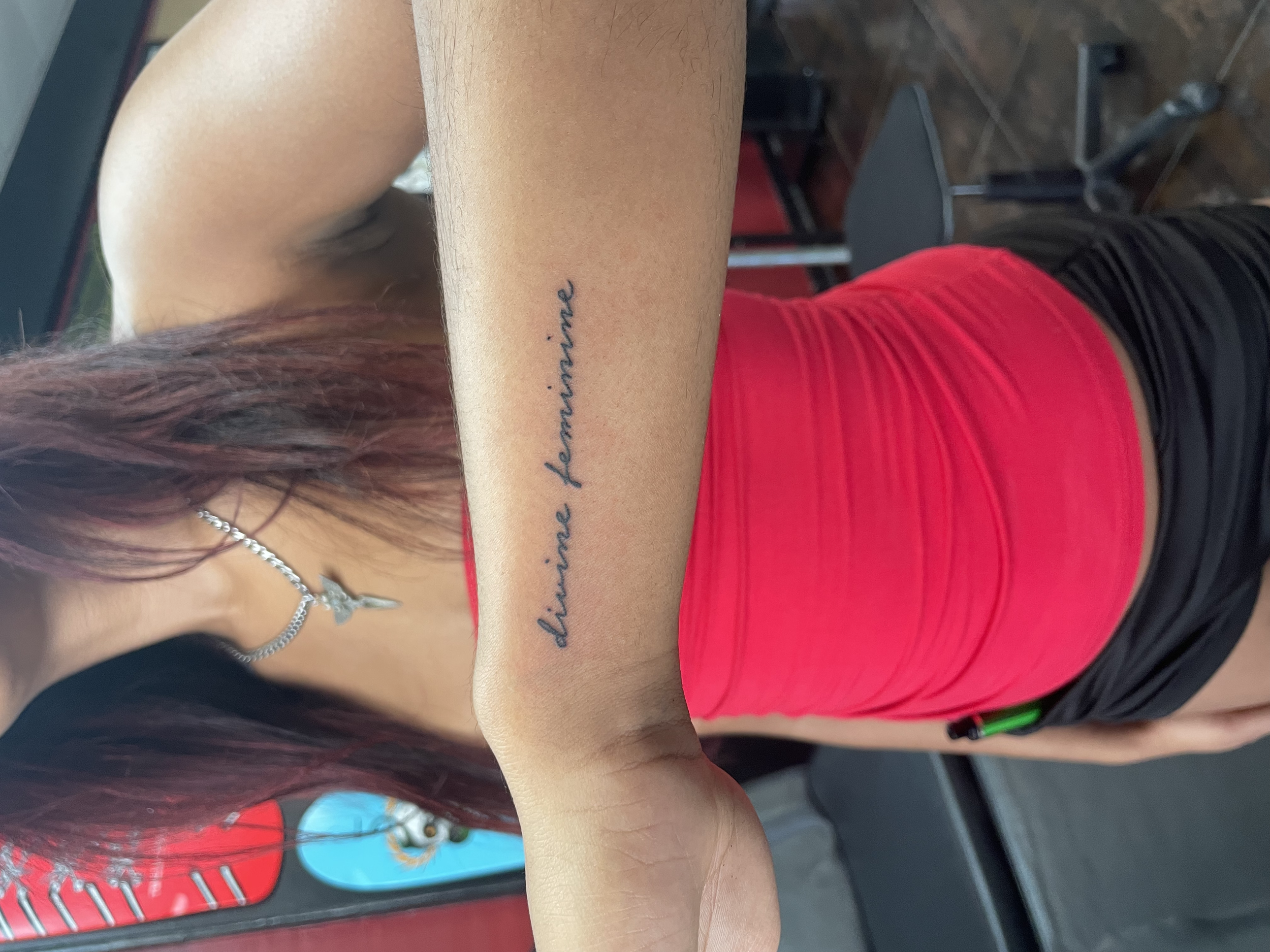 Fine line script tattoo reading "divine feminine" in elegant cursive lettering on the inner wrist. Custom fine line tattoo by Nick at Big Kahuna Tattoo in Boca Raton, FL.