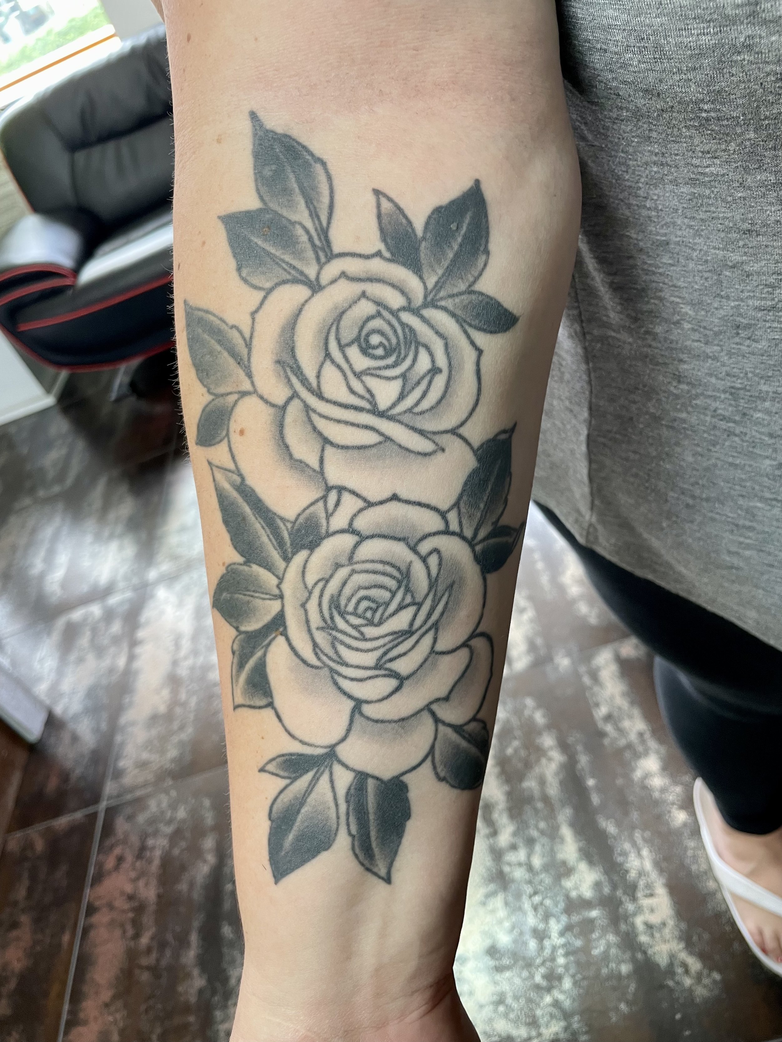 Two full bloom roses stacked vertically down the forearm, each with layered open petals and deep dark leaves. Classic subject matter executed with the kind of clean shading that only comes from real experience. Black and grey forearm tattoo by Nick a