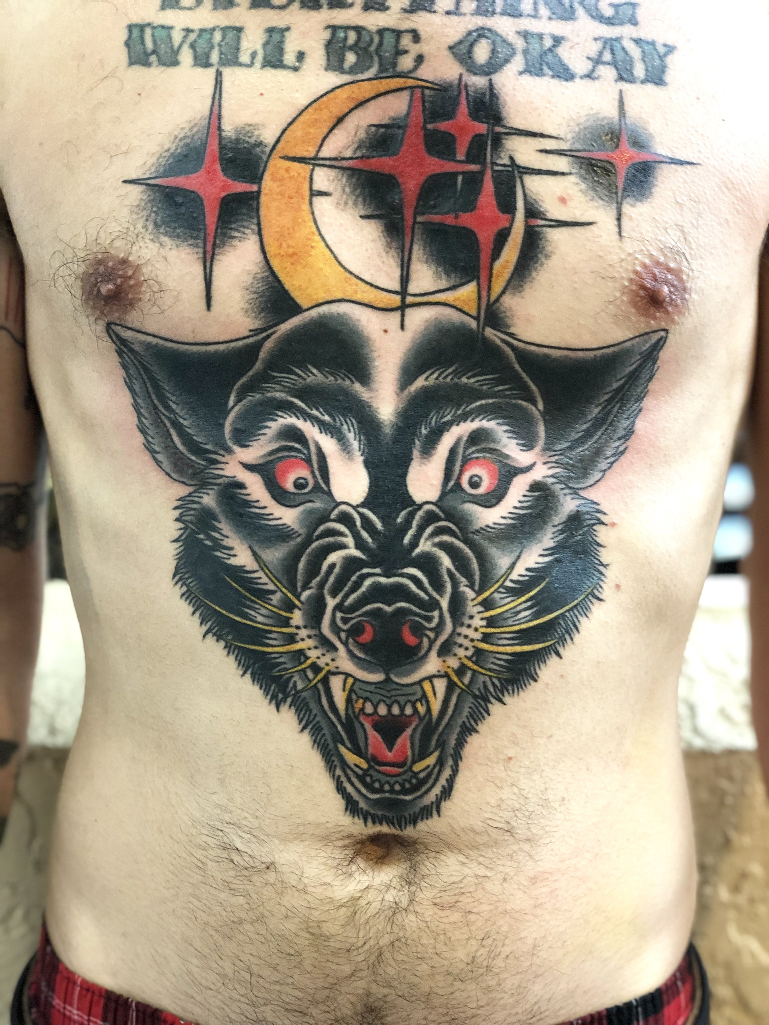 
Large traditional American color stomach tattoo featuring a snarling wolf head with red eyes and gold whiskers, set beneath a gold crescent moon flanked by bold red stars, custom tattoo by Nick at Big Kahuna Tattoo in Boca Raton, FL.