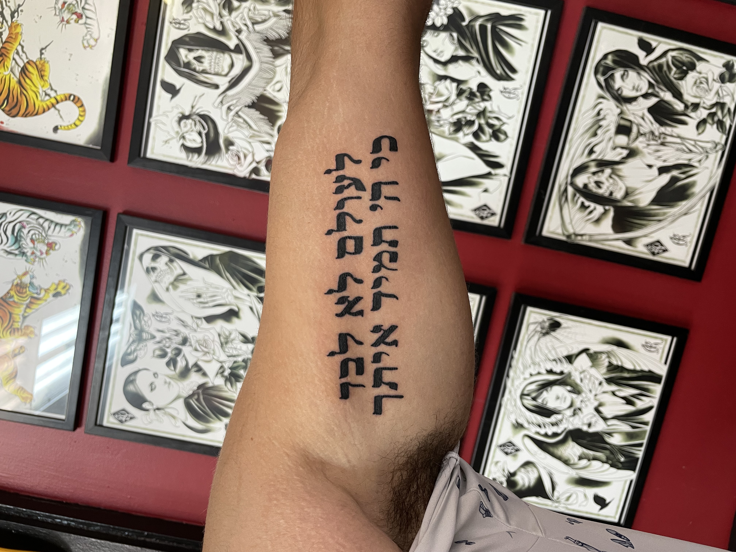 Bold black Hebrew script forearm tattoo reading "לעולם לא לבד כי ה' תמיד איתך" meaning "Never alone, for God is always with you," custom Hebrew lettering tattoo by Nick at Big Kahuna Tattoo in Boca Raton, FL.