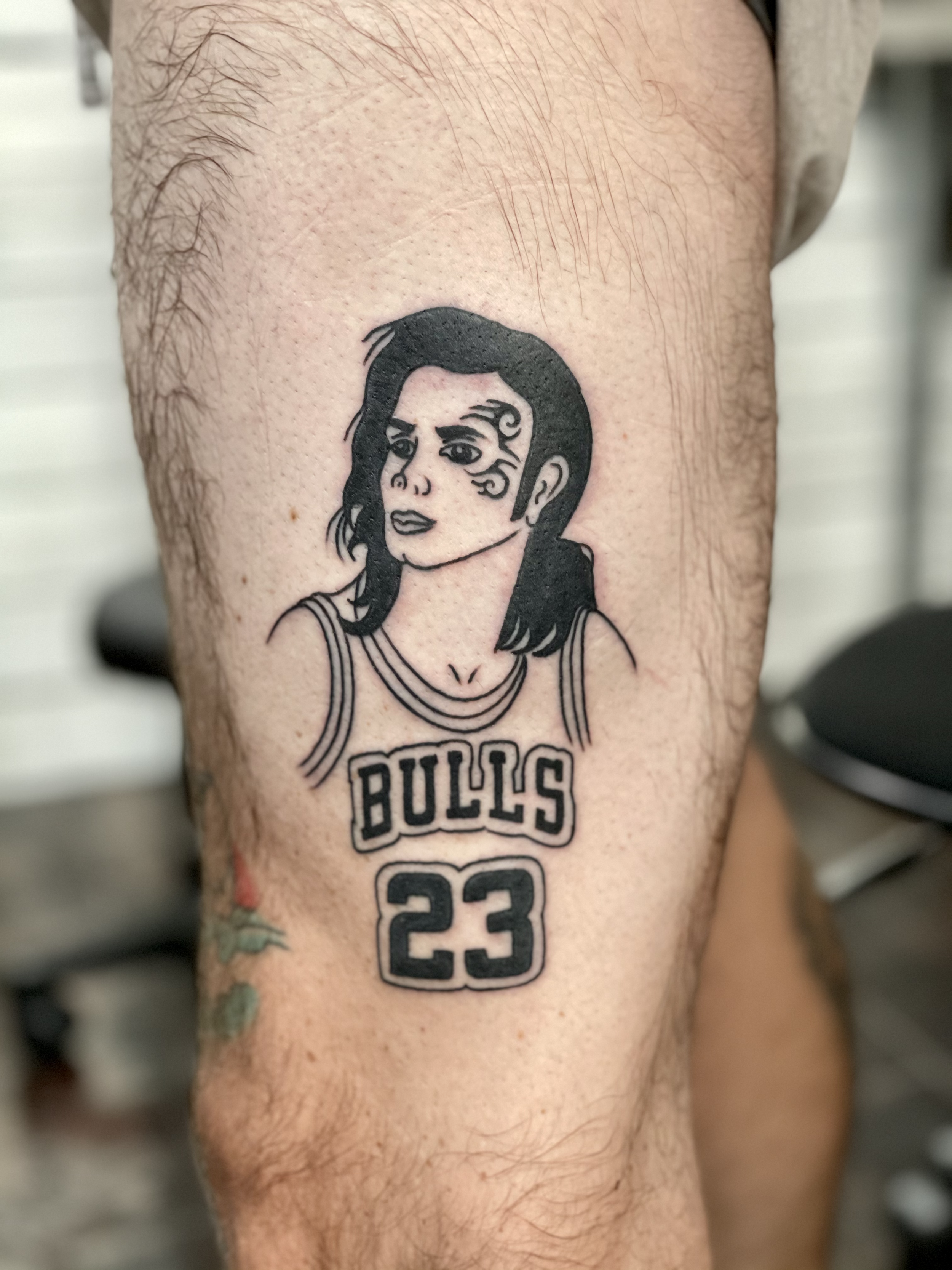 Humorous black and grey leg tattoo combining three iconic Michaels into one image — Michael Jackson's face and hair, wearing Michael Jordan's Chicago Bulls number 23 jersey, with Mike Tyson's famous facial tattoo, a creative pop culture mashup by Nic