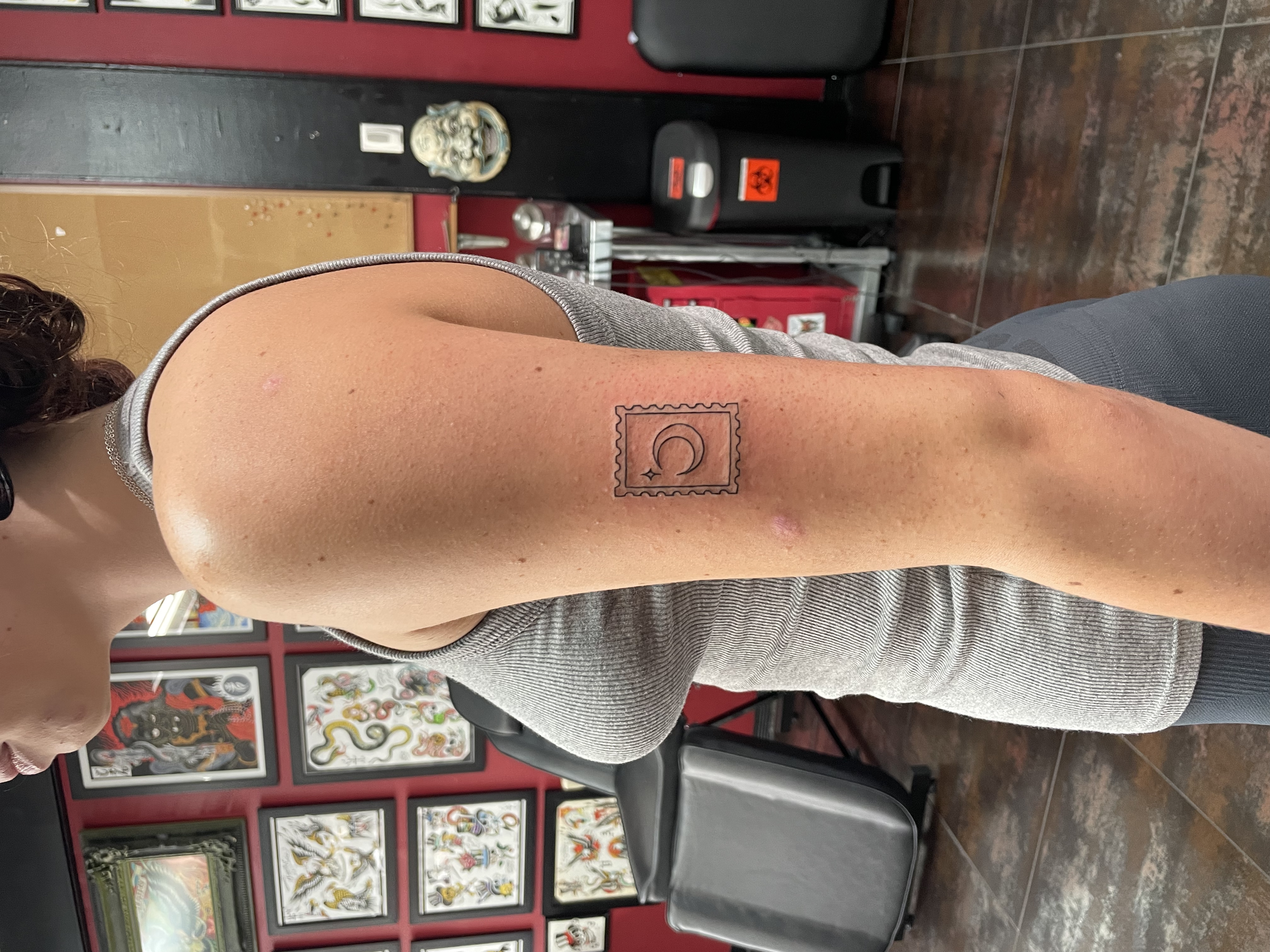 Minimalist fine line upper arm tattoo featuring a postage stamp design with a crescent moon and star, custom tattoo by Nick at Big Kahuna Tattoo in Boca Raton, FL.