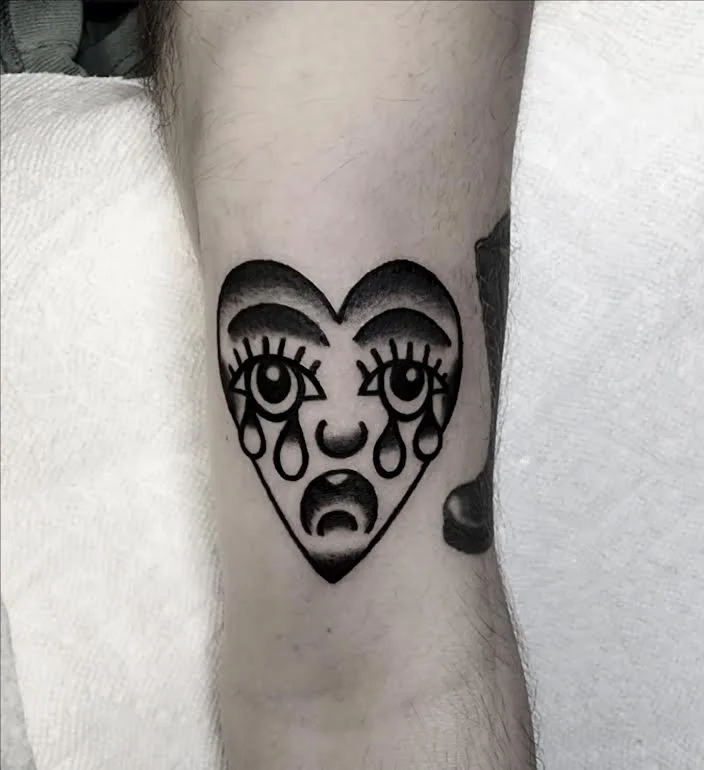 Black and grey traditional arm tattoo featuring a bold crying heart face with expressive eyes and tears, custom tattoo by Brandon Perez at Big Kahuna Tattoo in Boca Raton, FL
