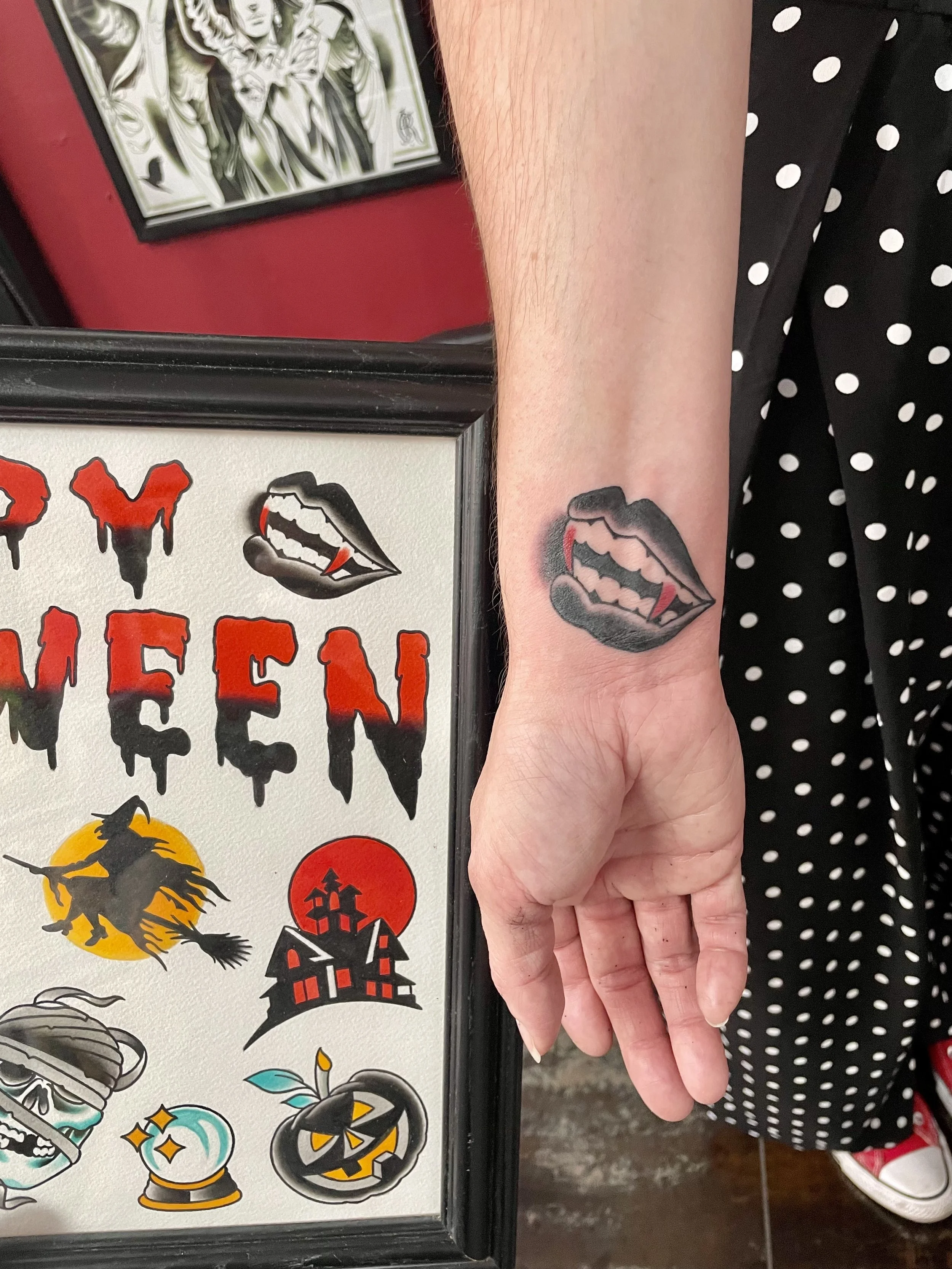 
Traditional American black and grey wrist tattoo featuring a bold pair of vampire lips with glistening fangs and red blood drops pictured next to the piece of flash the tattoo is referencing, custom tattoo by Nick at Big Kahuna Tattoo in Boca Raton,