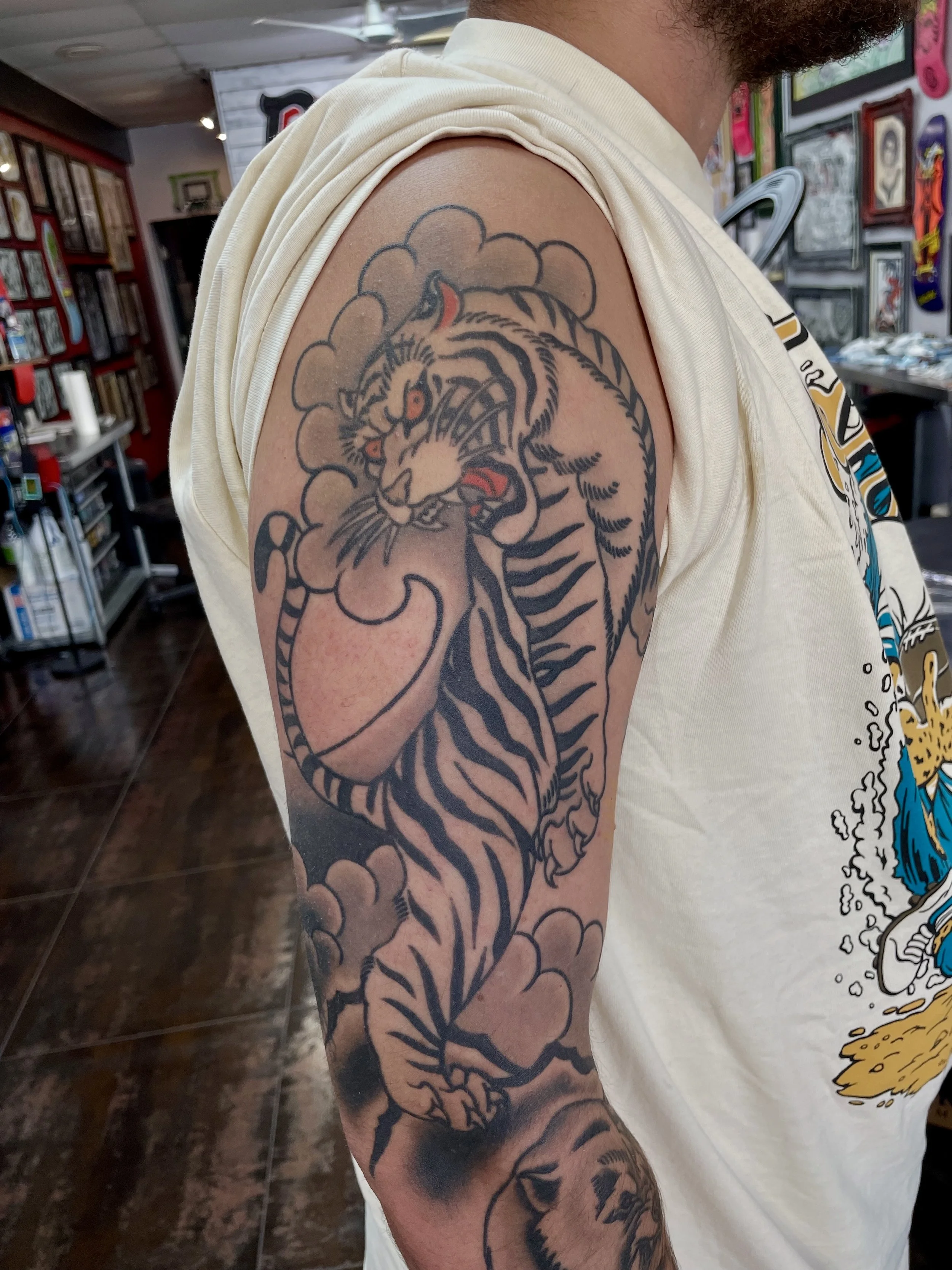 A white tiger with bold black stripes emerges from billowing wind clouds that wrap the full length of the upper arm. One of the most enduring images in Japanese tattooing, executed in a way that you can see. Japanese sleeve tattoo by Nick at Big Kahu