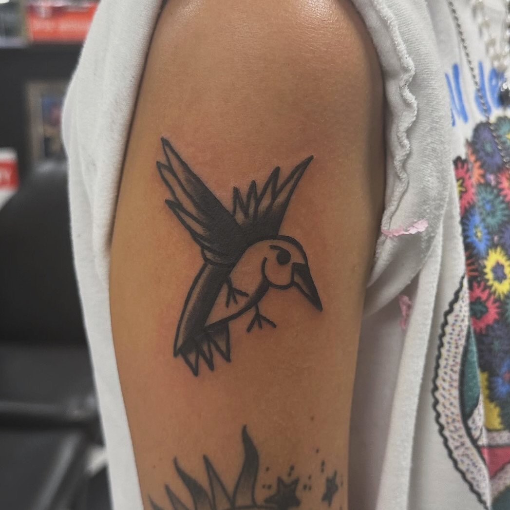 Traditional American black and grey upper arm tattoo featuring a bold flying hummingbird in mid-wingbeat with strong linework and smooth shading, custom tattoo by Dan at Big Kahuna Tattoo in Boca Raton, FL.