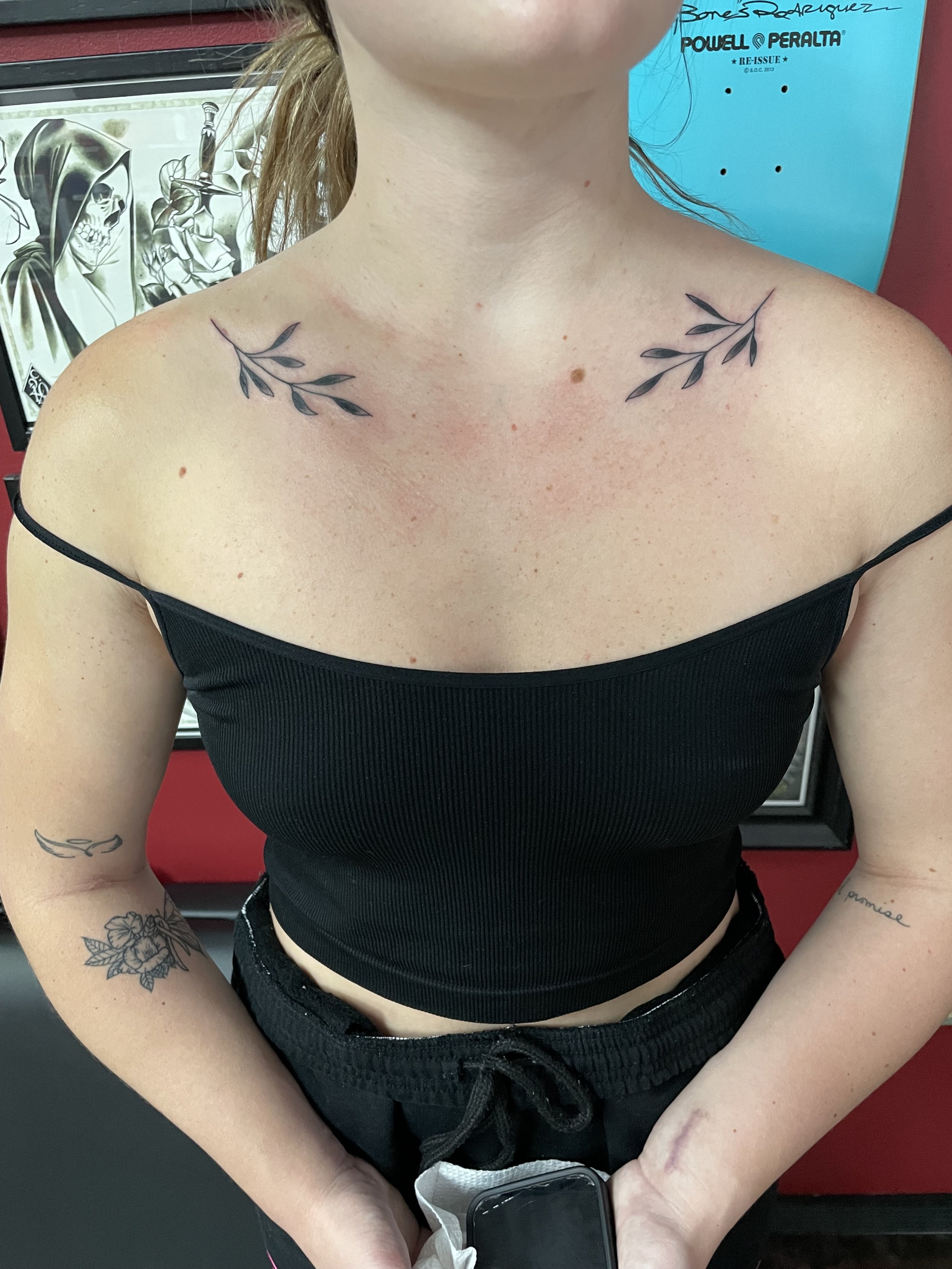 Fine line matching collarbone tattoos featuring a delicate olive branch with small pointed leaves placed symmetrically on each collarbone, custom tattoo by Nick at Big Kahuna Tattoo in Boca Raton, FL.