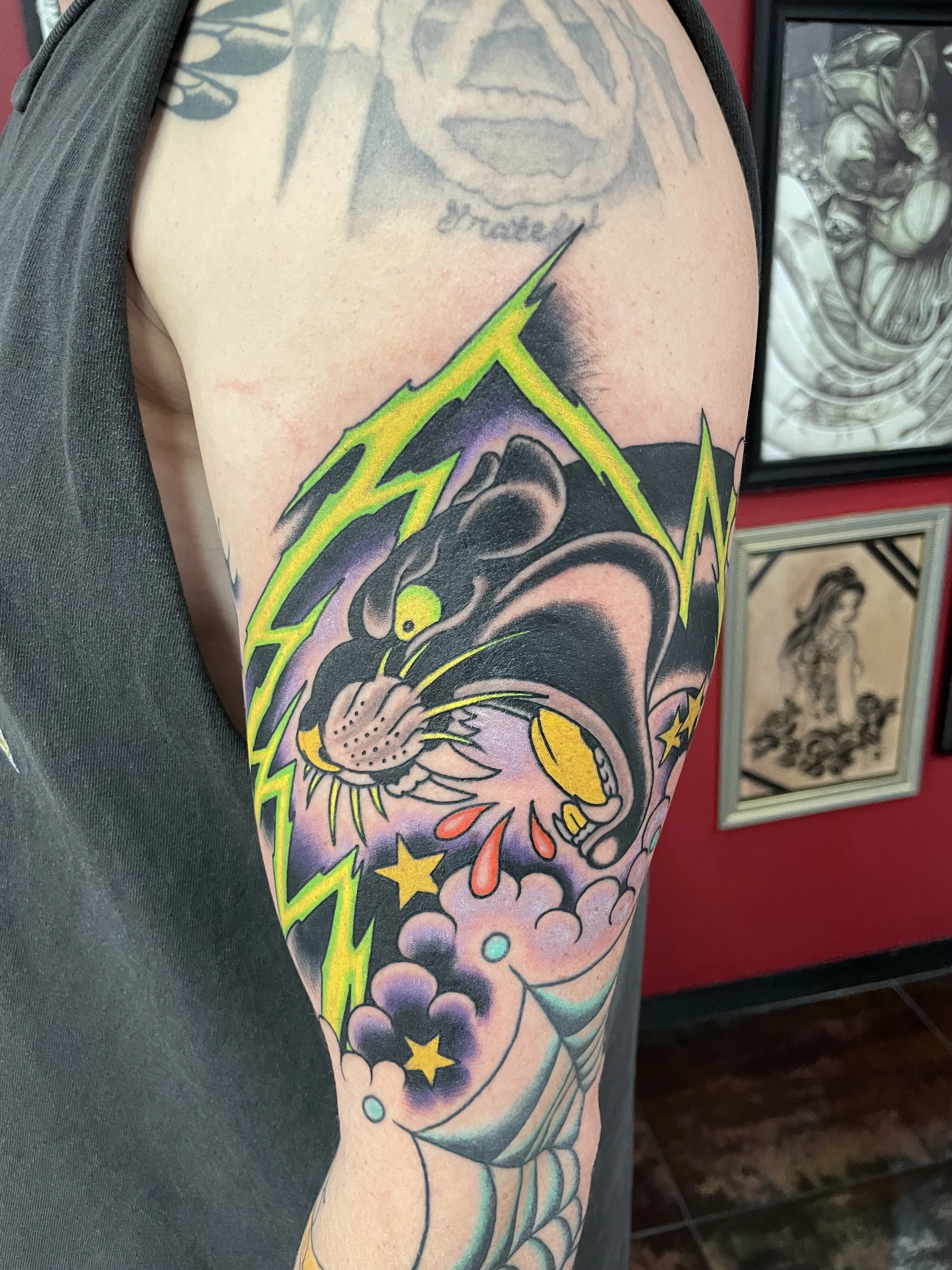Traditional American color upper arm tattoo featuring a snarling black panther with a glowing yellow eye and red blood drops, surrounded by bold neon green lightning bolts, purple clouds, and gold stars on a deep shadowed background, custom tattoo by
