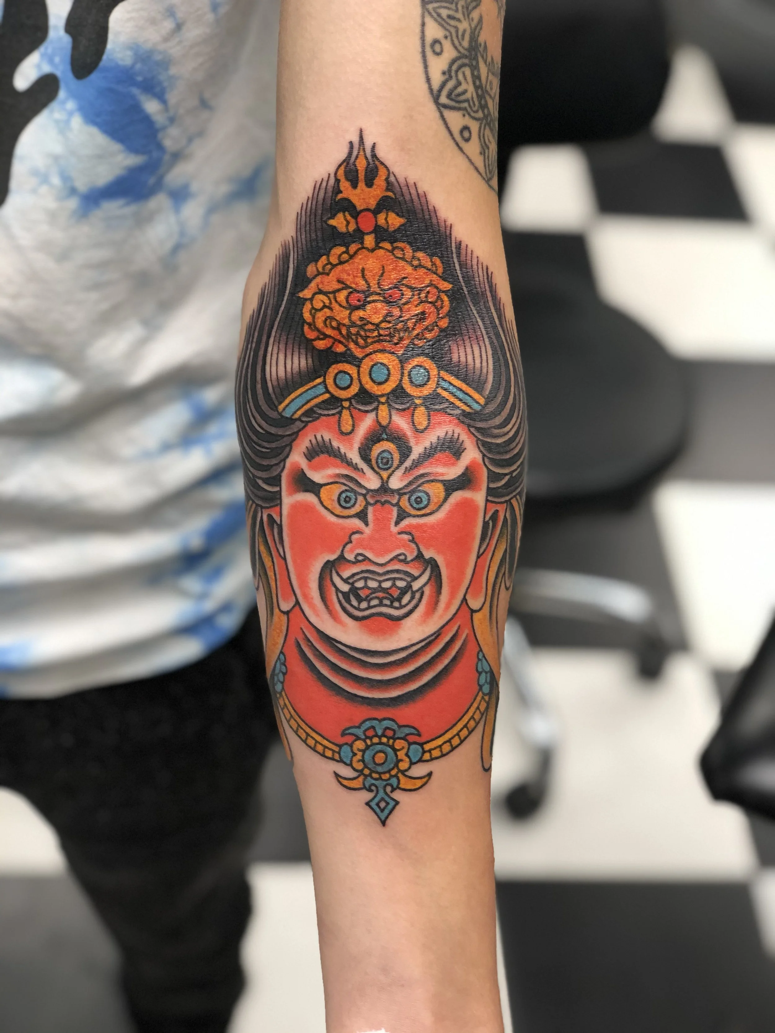 Traditional Japanese color forearm tattoo featuring Kongo Zao Gongen, the powerful syncretic deity of Japanese Buddhism and Shintoism, depicted with a fierce red face, third eye, ornate orange headdress with a vajra, and teal and gold decorative deta