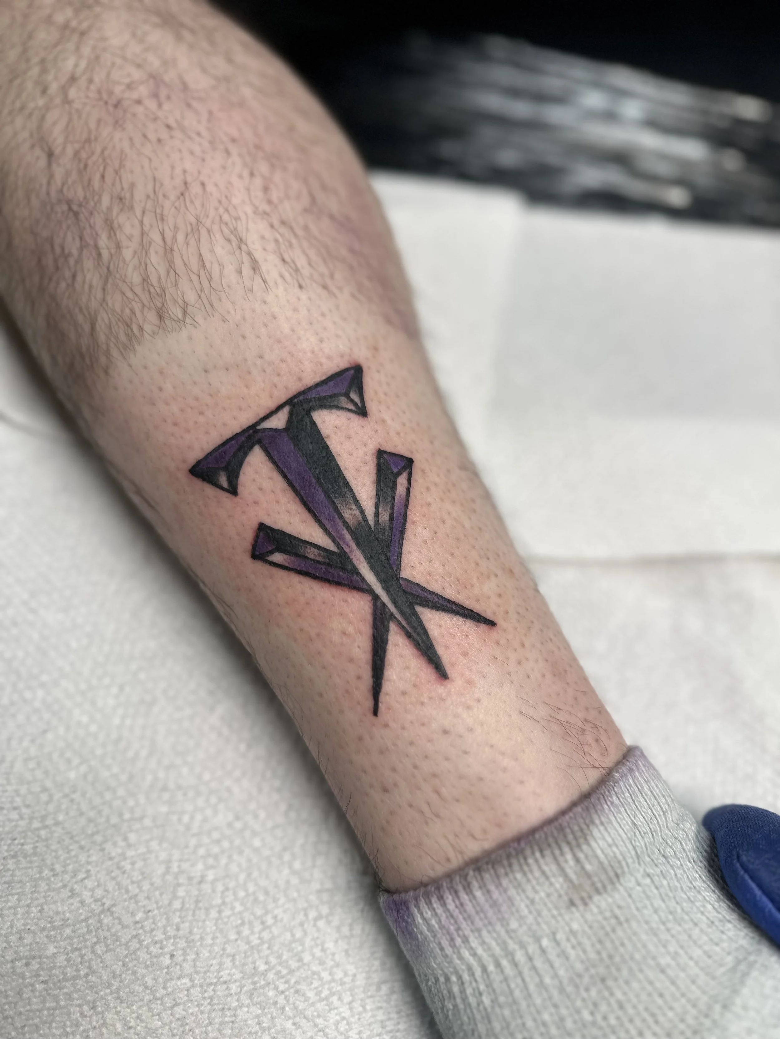 Traditional American black and grey forearm tattoo featuring the Undertaker's iconic logo from WWF with purple accents and bold geometric linework, custom tattoo by Dan at Big Kahuna Tattoo in Boca Raton, FL.
