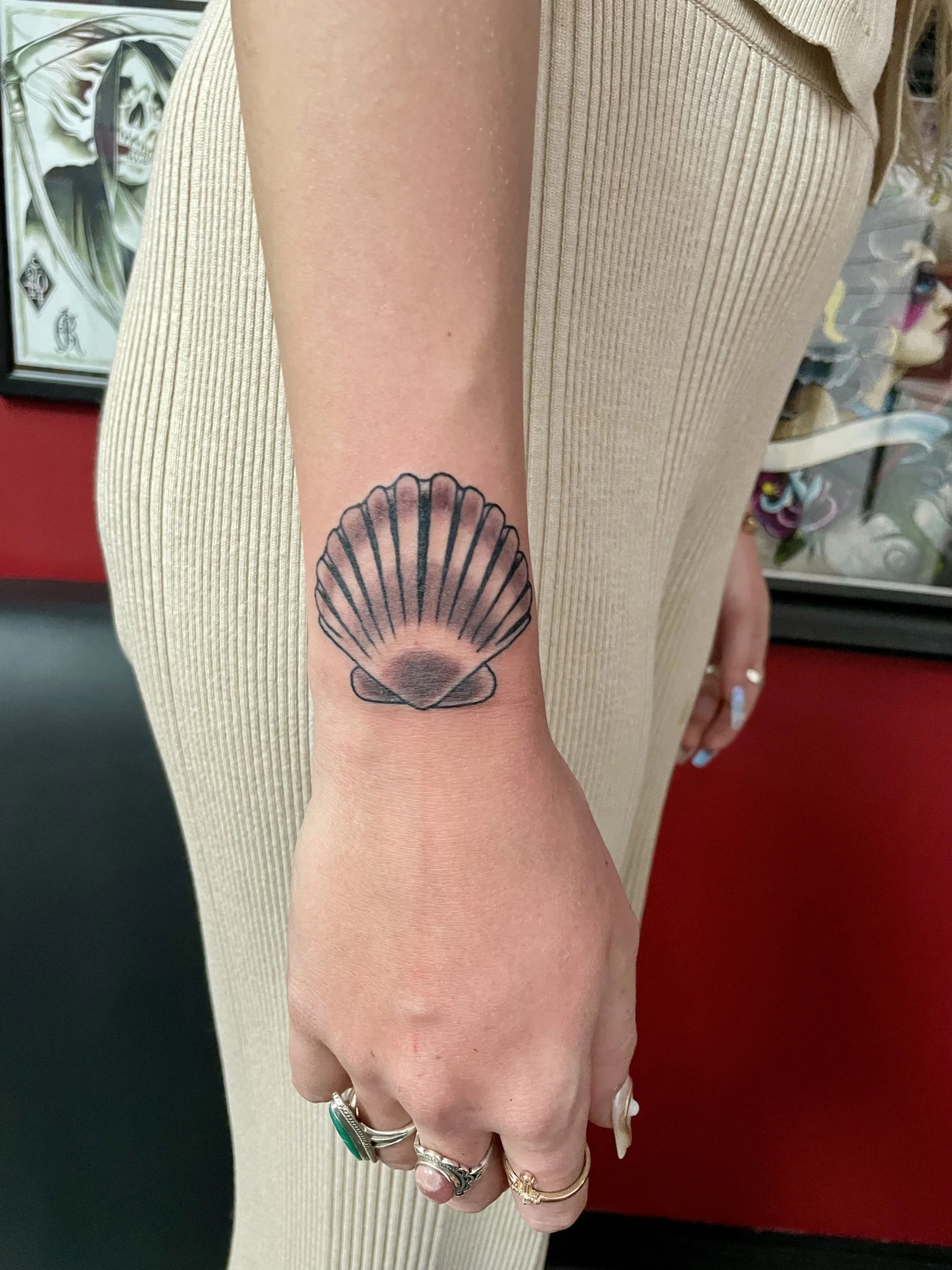 Fine line black and grey wrist tattoo featuring a classic scallop seashell with detailed radiating ridges and soft shading, custom tattoo by Nick at Big Kahuna Tattoo in Boca Raton, FL.