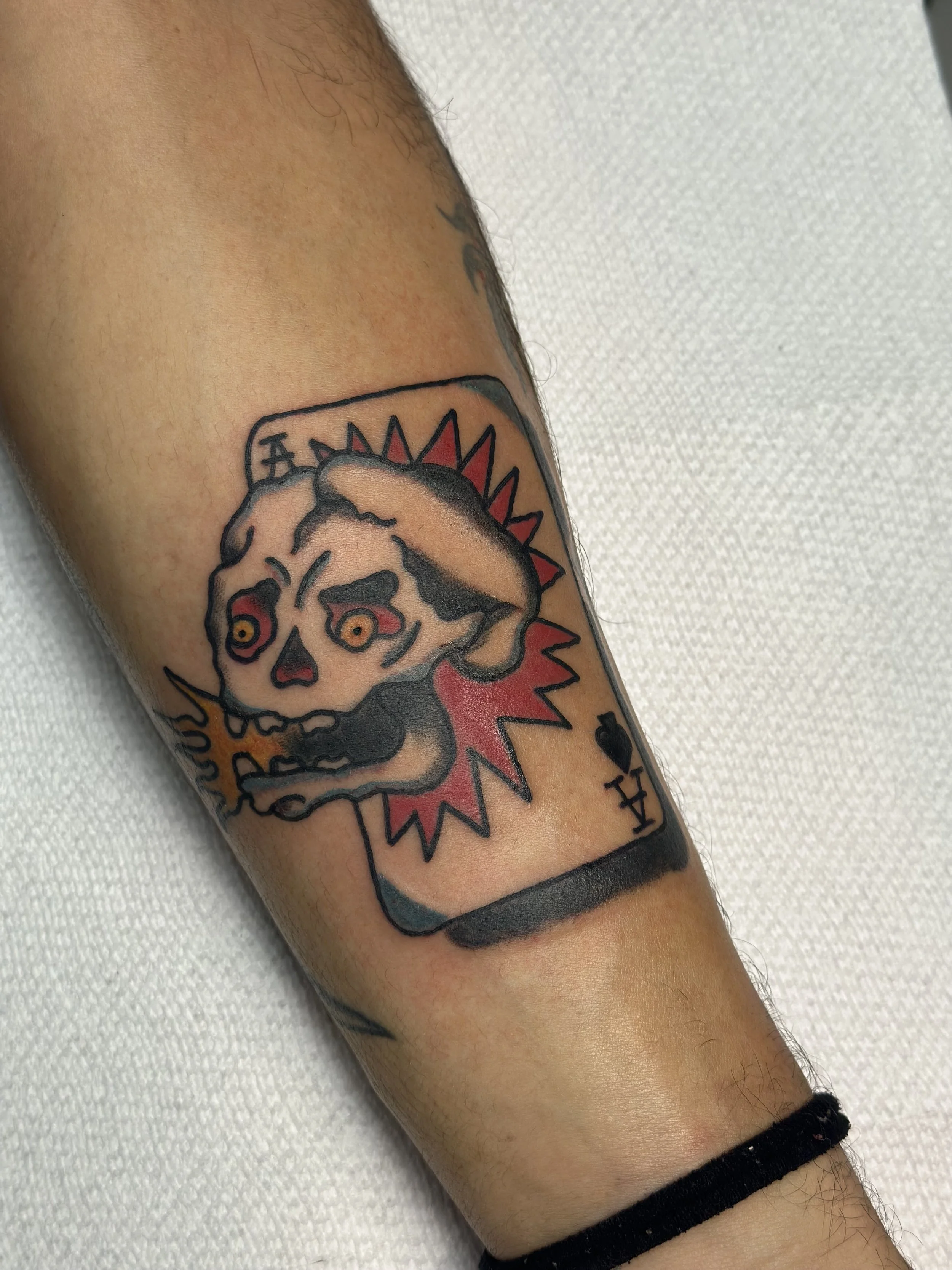 Traditional American color forearm tattoo featuring a skull exploding through an ace of spades playing card with a red explosion and yellow eyes, custom tattoo by Dan at Big Kahuna Tattoo in Boca Raton, FL.