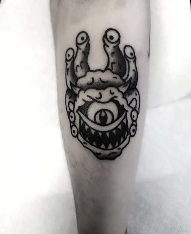 Bold black and grey traditional leg tattoo featuring a Beholder from Dungeons and Dragons with a large central eye, multiple eye stalks and sharp teeth, custom D&D tribute tattoo by Brandon Perez at Big Kahuna Tattoo in Boca Raton, FL